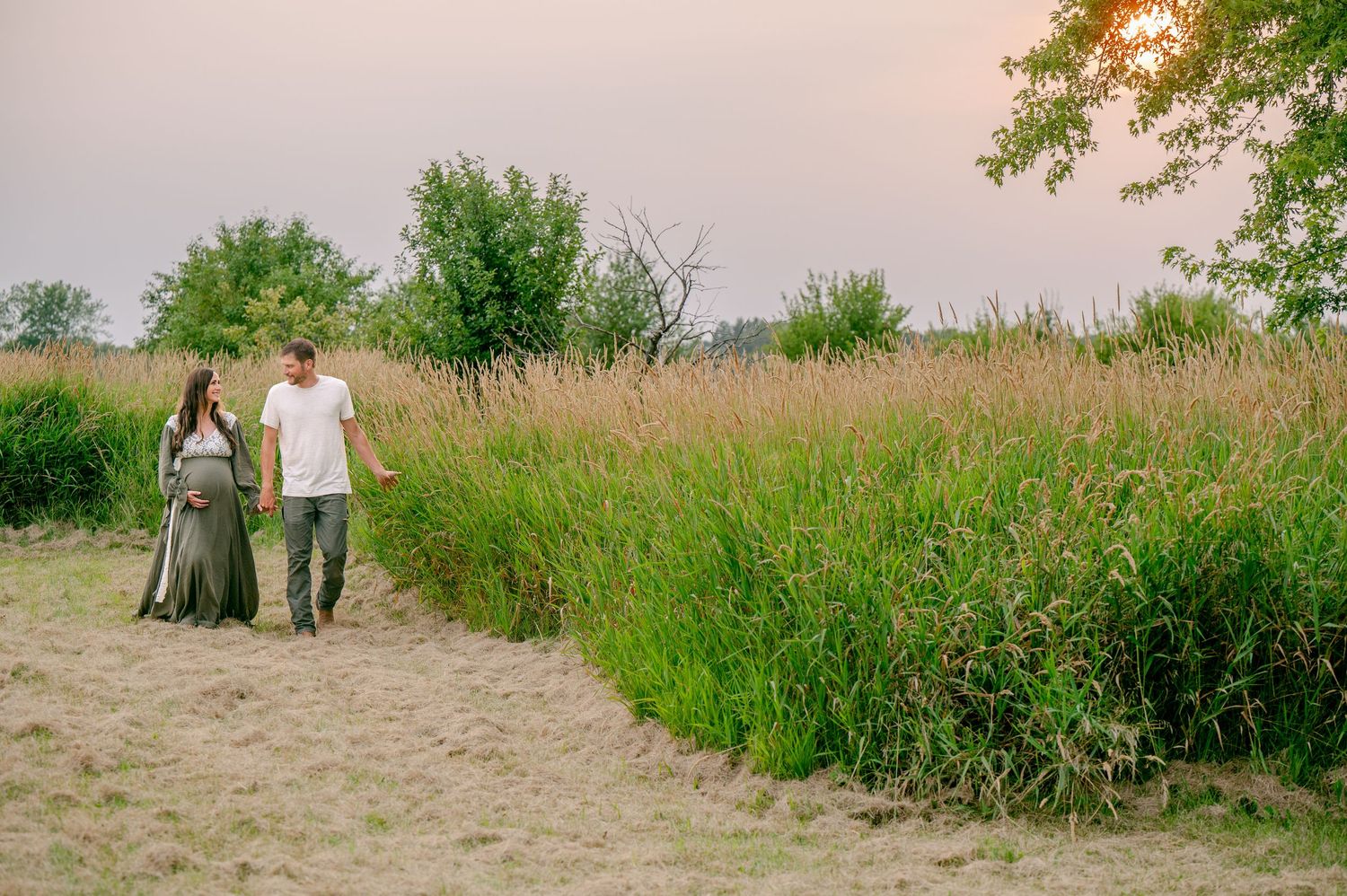 Silhouetted couple walking hand in hand through a sunlit meadow path during sunset.