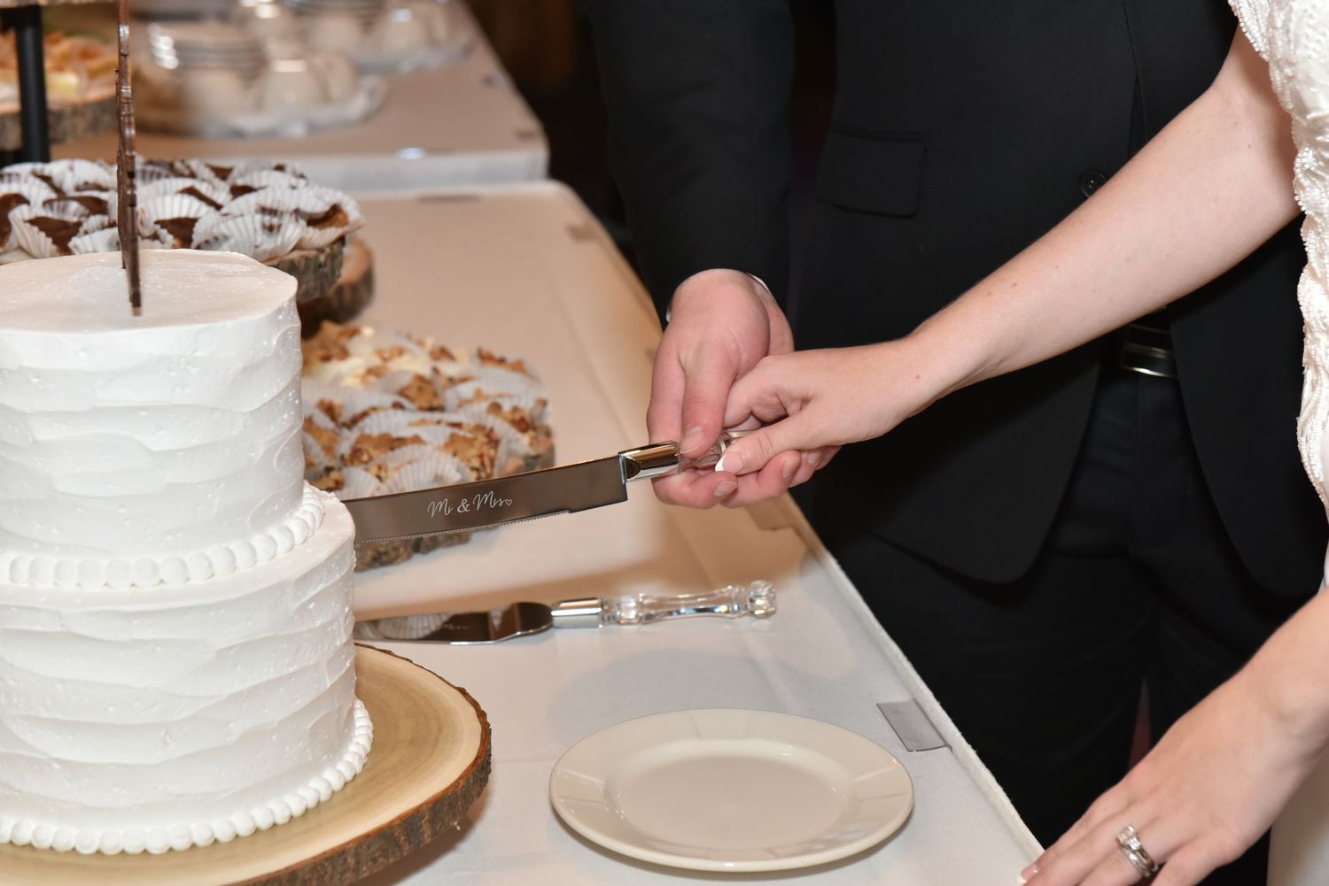 The Grands At Mulligans. Close-up of white wedding cake being cut at reception with traditional pearl decorations.