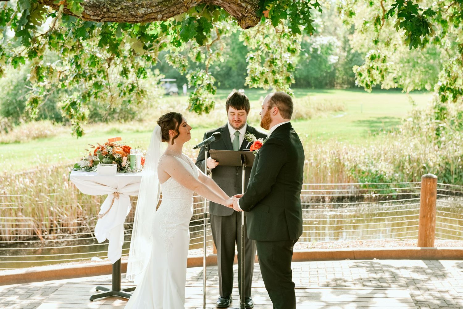 Wedding couple and attendants gather under green foliage for outdoor ceremony photos.