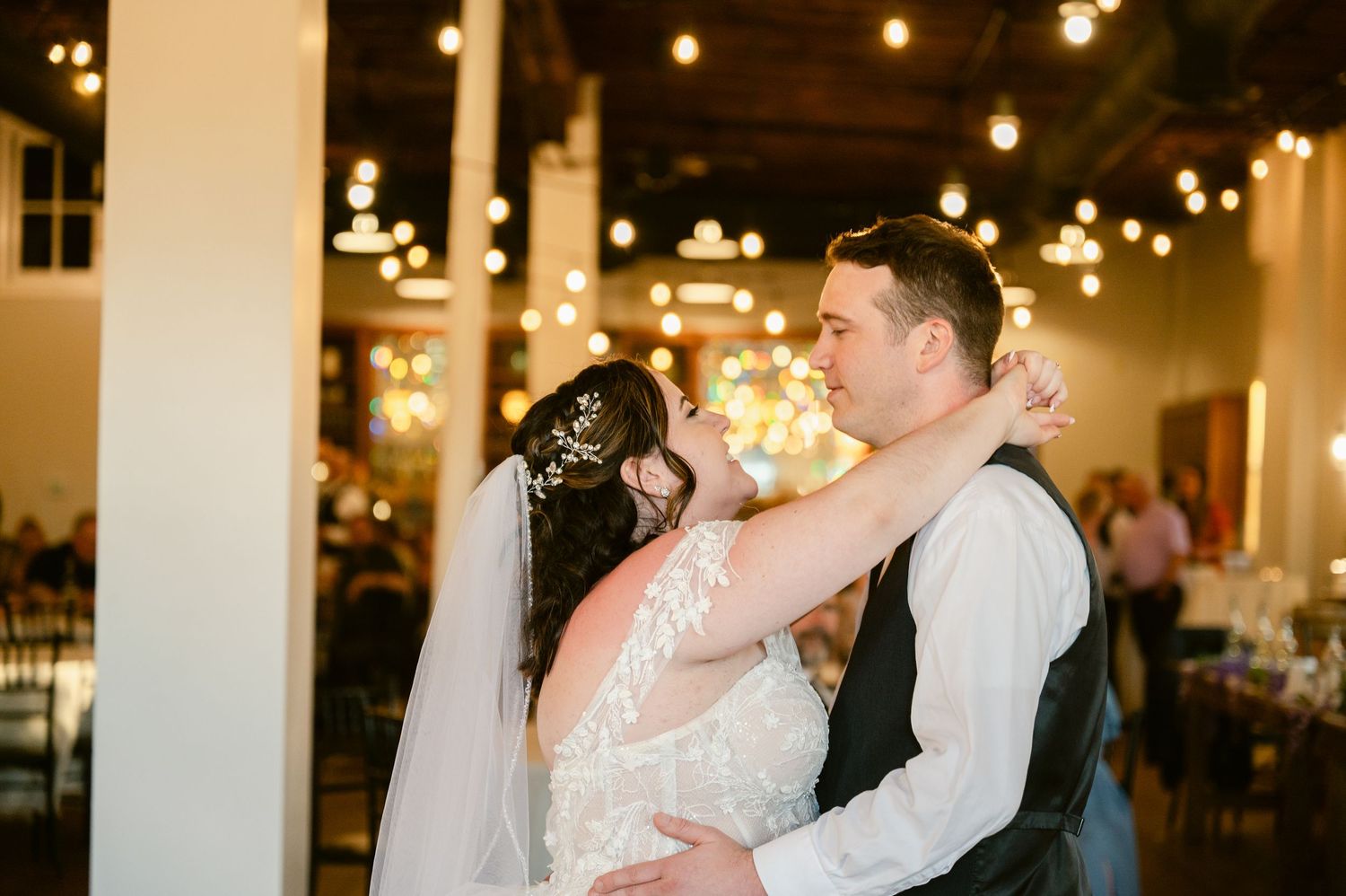 A couple shares their first dance under glowing string lights in an elegant reception venue.