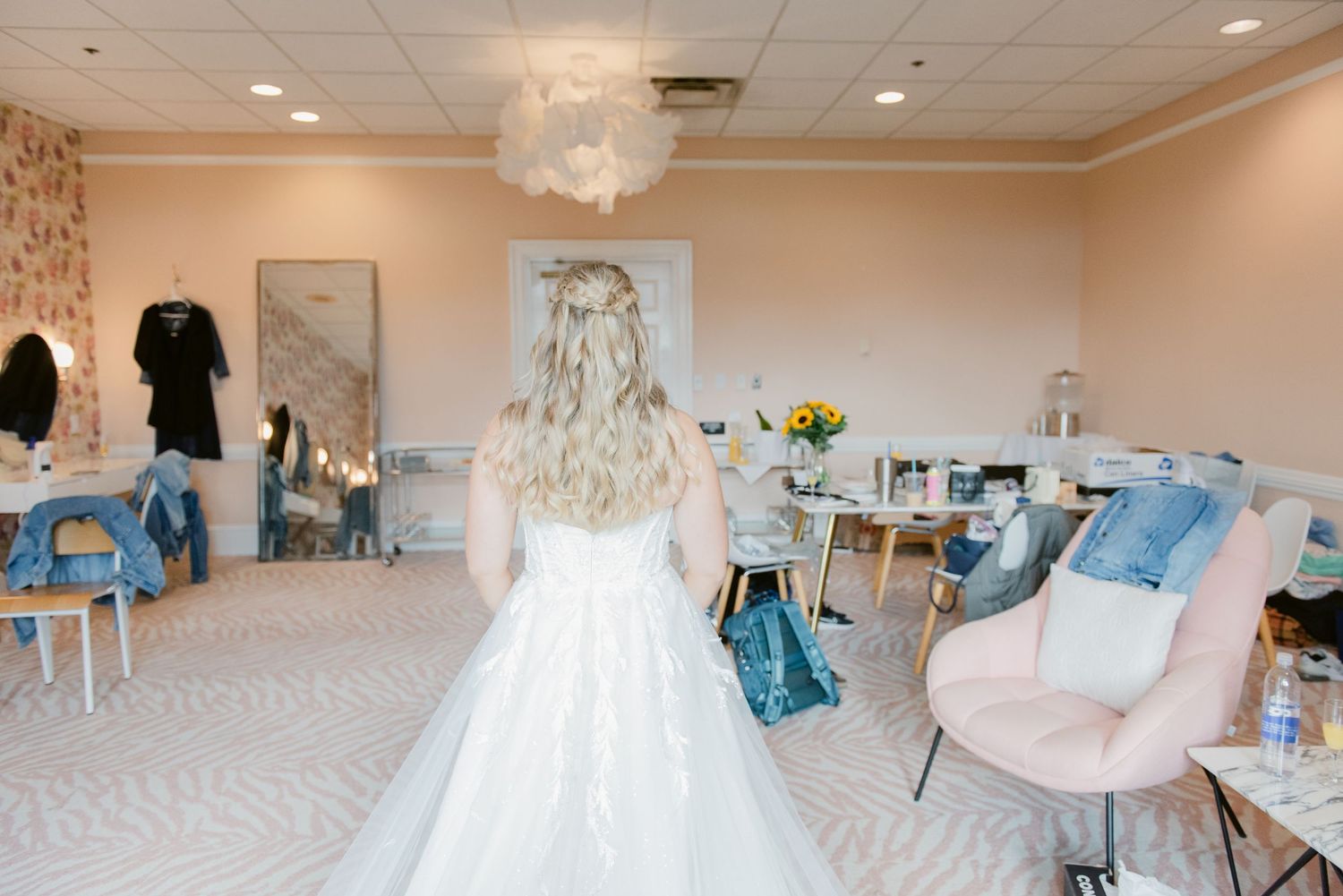 A bride in a white wedding dress stands in a getting ready room with blue decor.