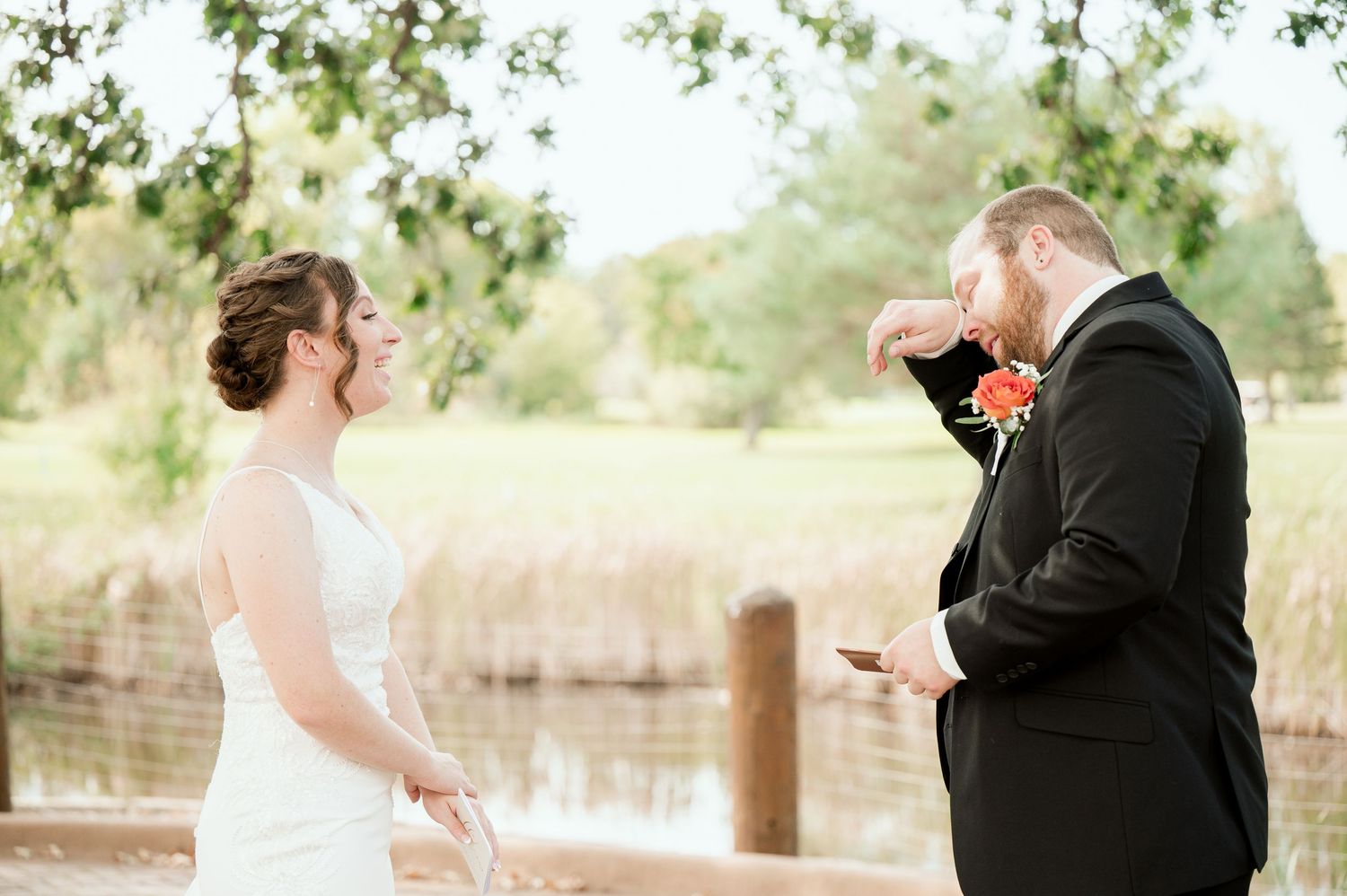 Two people in formal wedding attire share an emotional moment together on a dock by a lake.