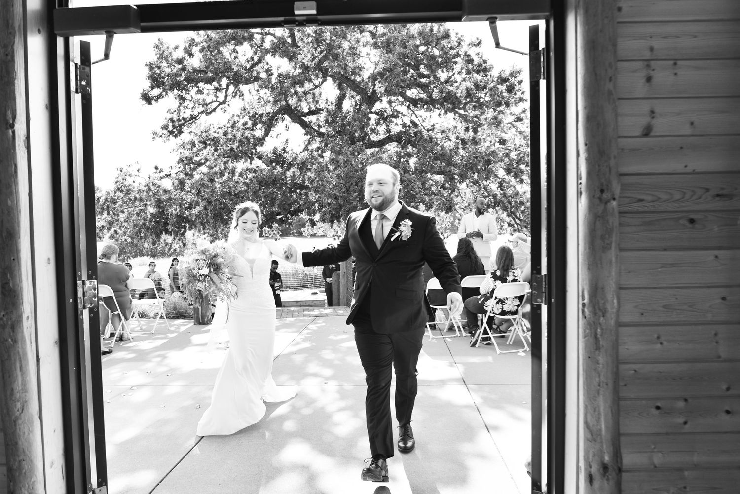 The Grands at Mulligans- Wedding Photos: A black and white capture of a wedding exit through rustic wooden doors.