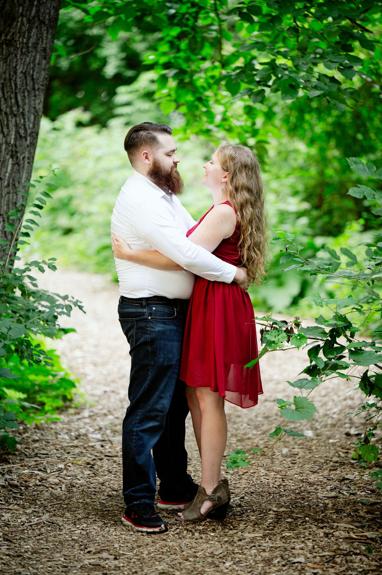 A romantic couple sharing tender moments among lush green trees on a forest path.