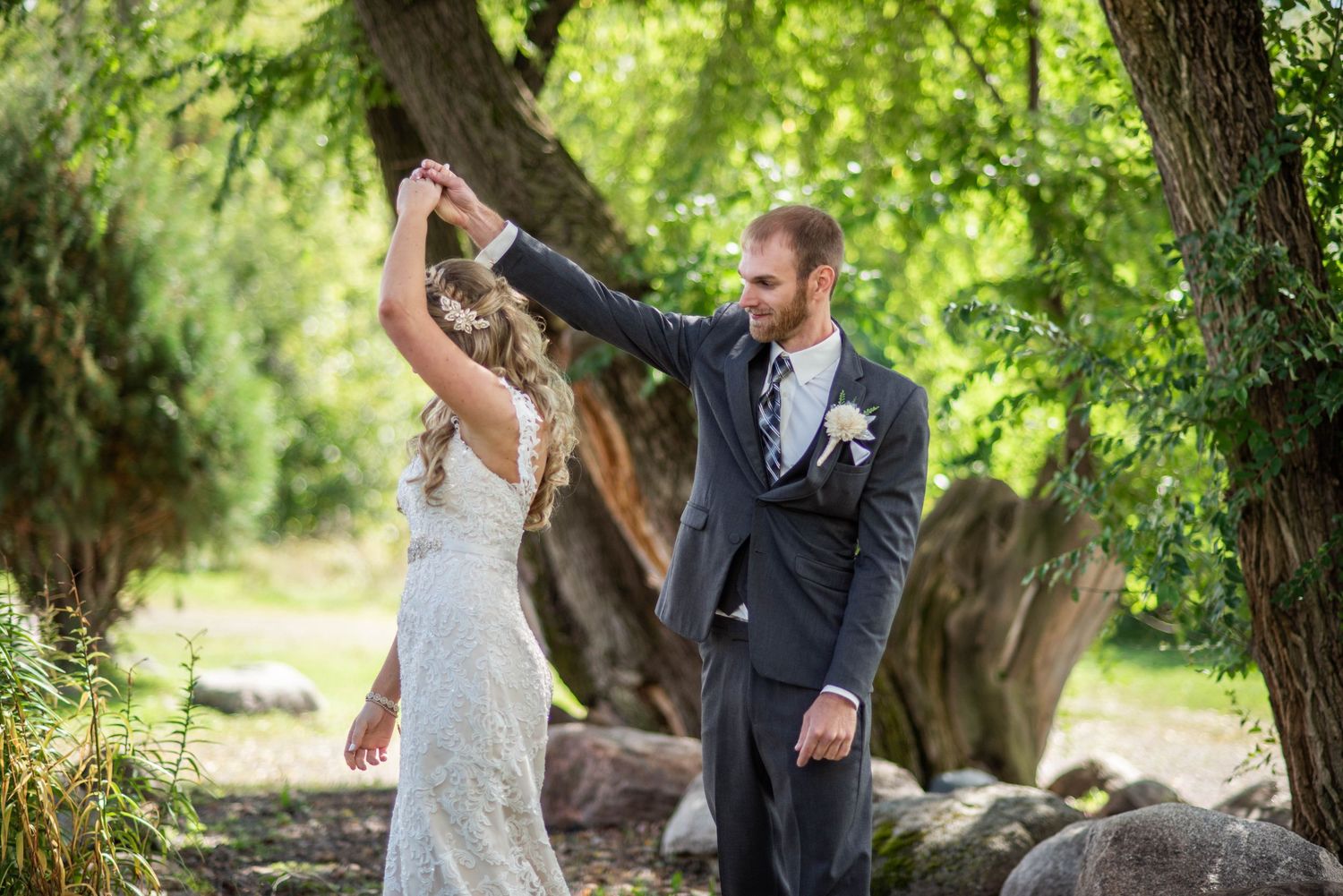 A newlywed couple dances together outdoors surrounded by trees and natural stone elements.
