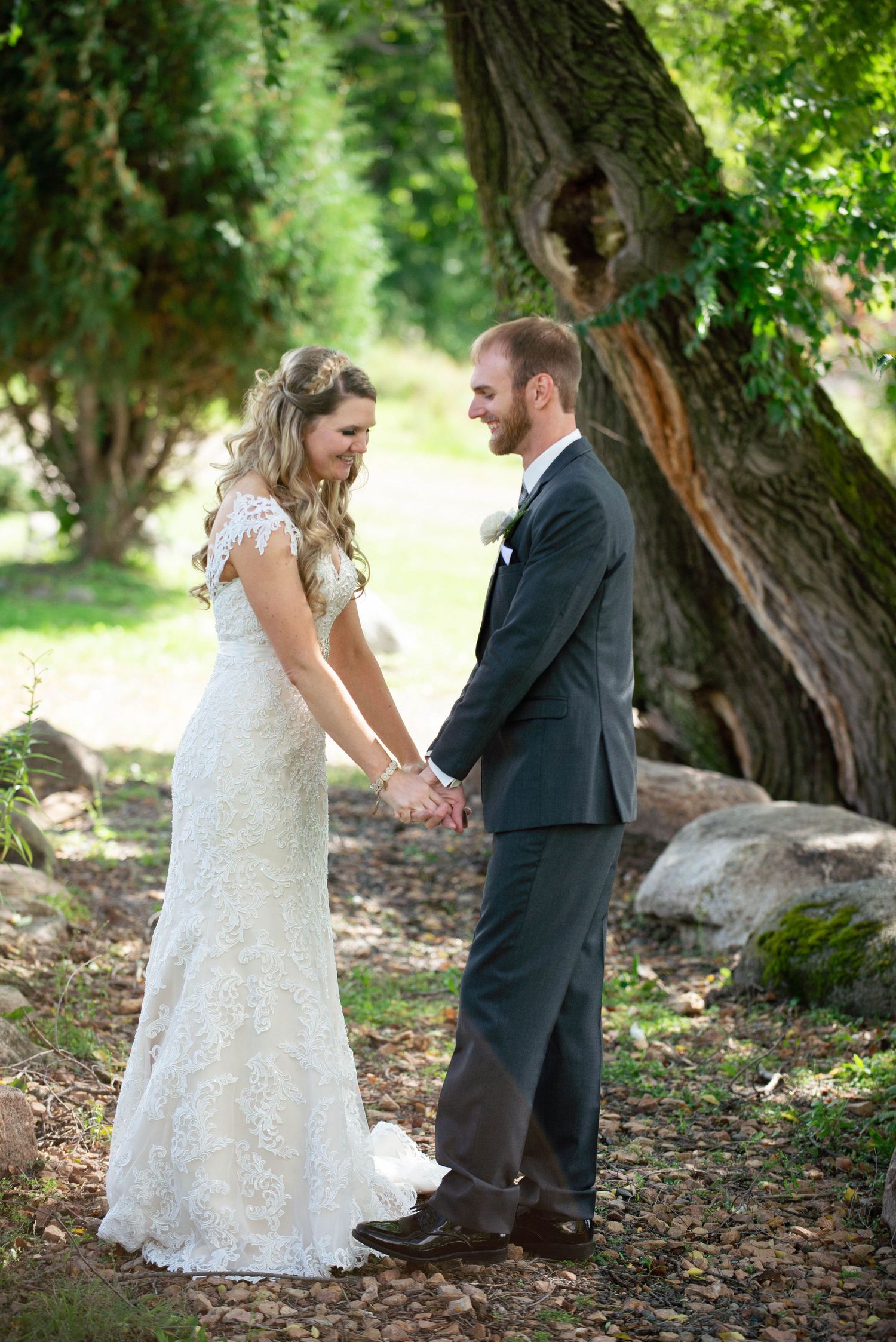 A wedding couple holds hands and gazes at each other beneath a towering tree. Rum River Barn Milaca Minnesota Weddings