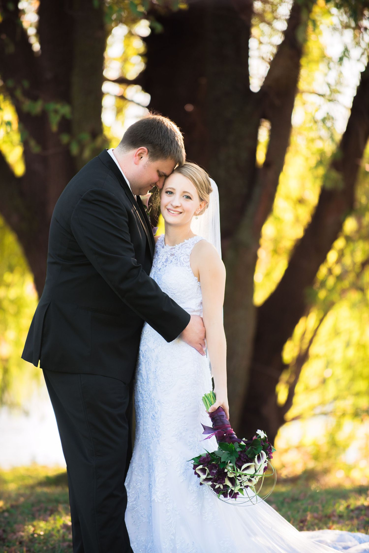 Romantic wedding portrait showing couple embracing outdoors with sunlit autumn trees in background. Andover wedding at Magestic Oaks Golf Cl