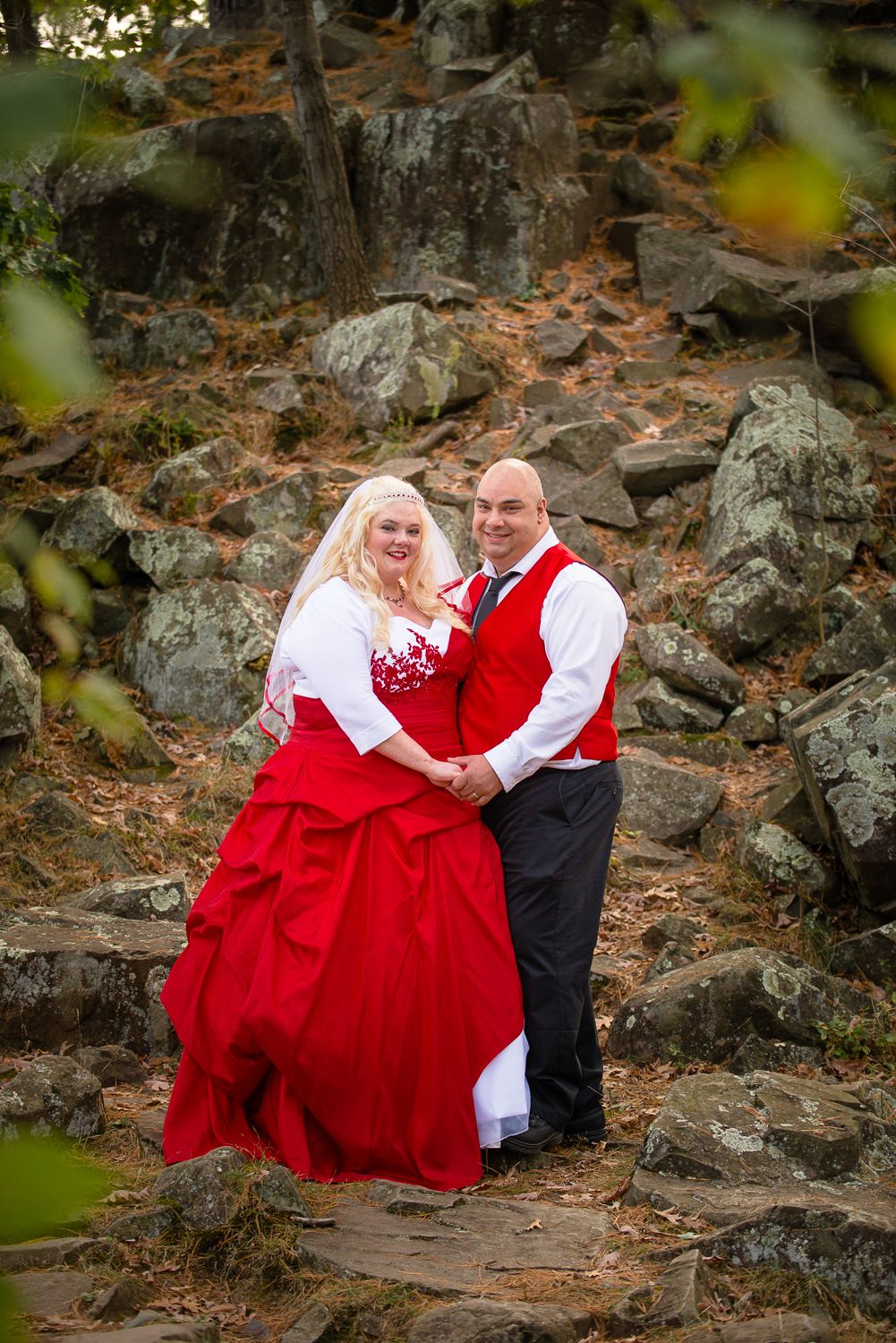 A couple in matching red and white outfits pose together on rocky terrain during an outdoor photo session.