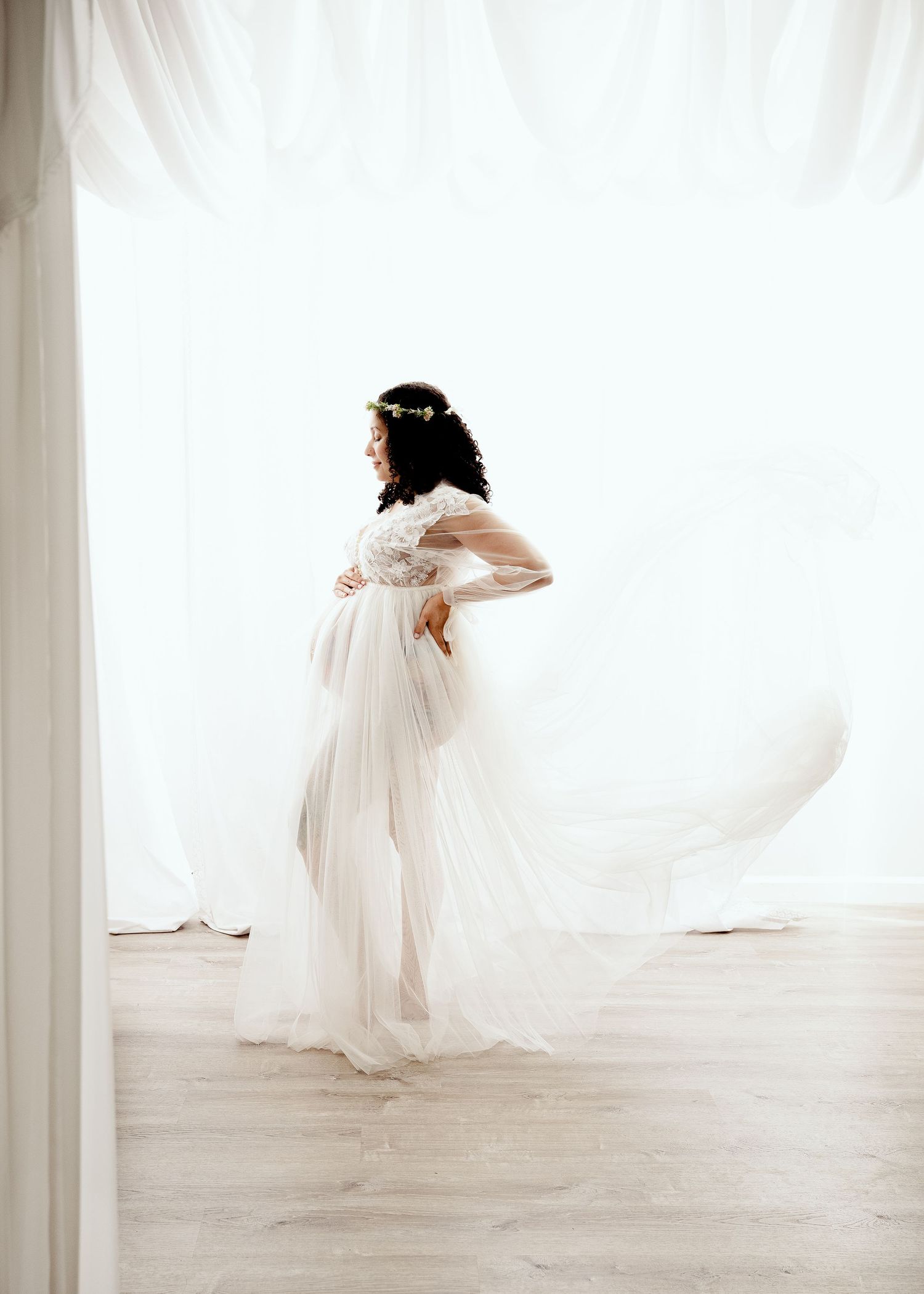 Elegant maternity photo featuring flowing white dress against light backdrop.