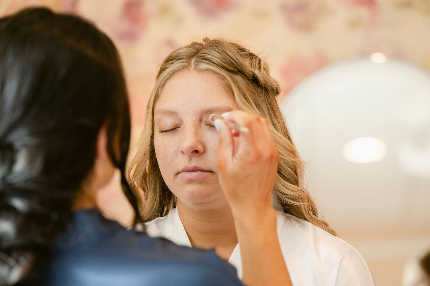 Makeup artist applying cosmetics during bridal preparation in soft lighting.