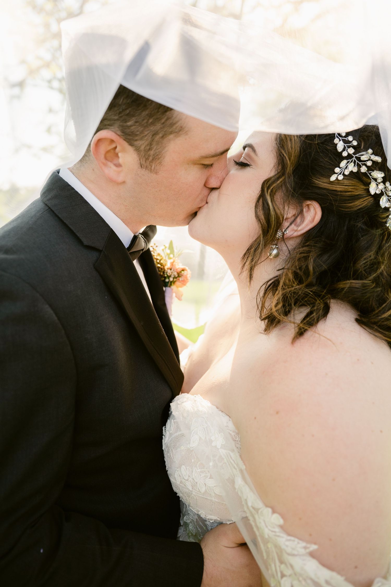 Romantic wedding day kiss captured in soft natural lighting with delicate floral details.
