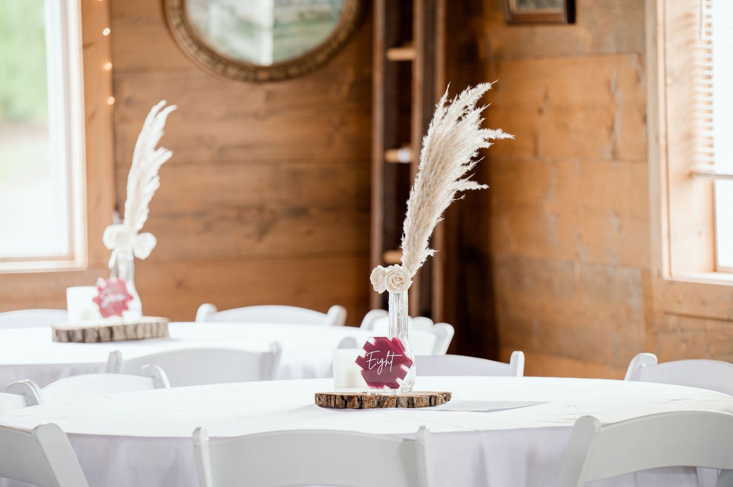 White feather plume centerpieces with purple flowers on rustic wood slices decorate tables at a wedding reception.