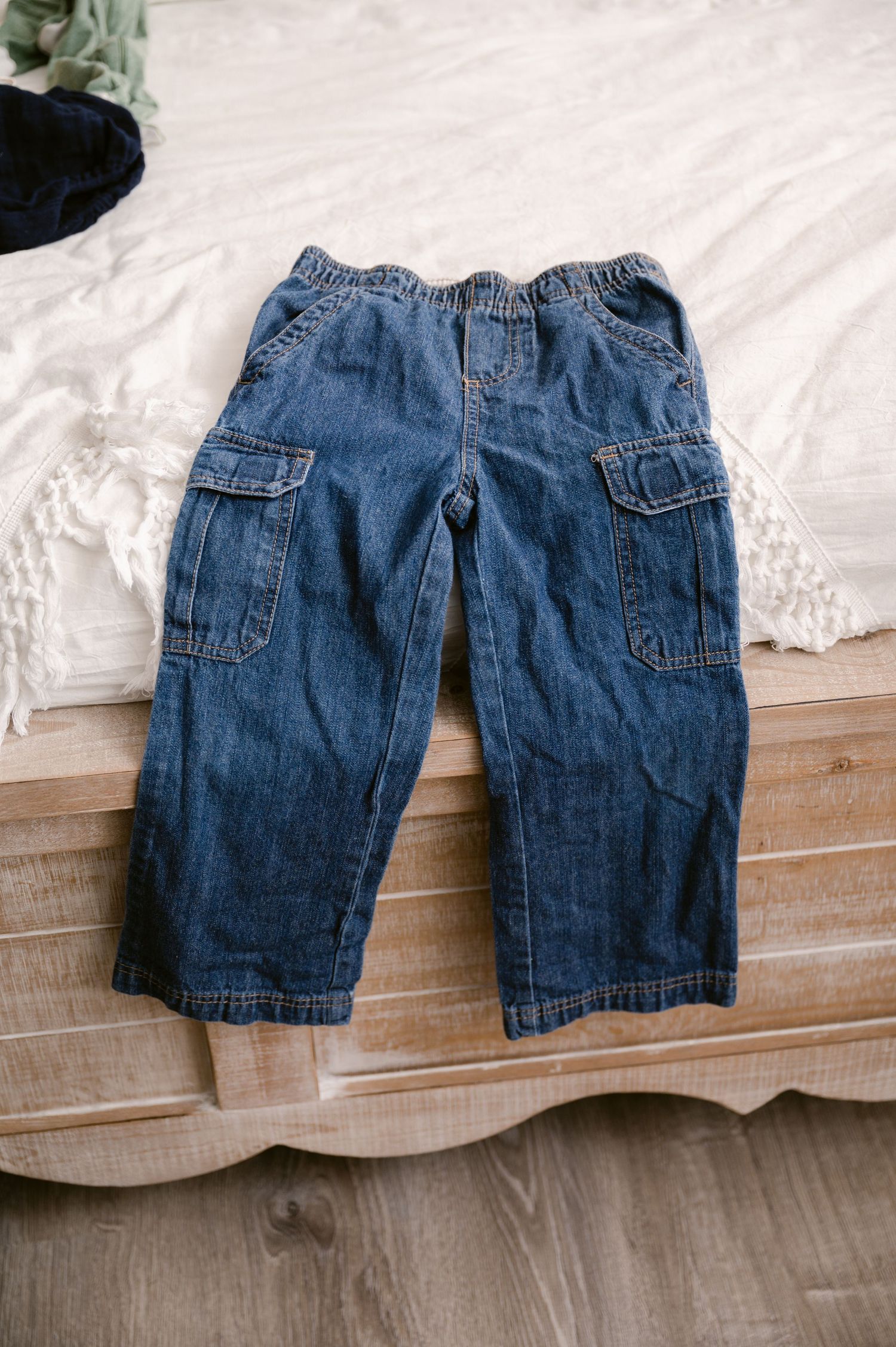 A pair of toddler's blue denim jeans with cargo pockets laid flat on a white surface.