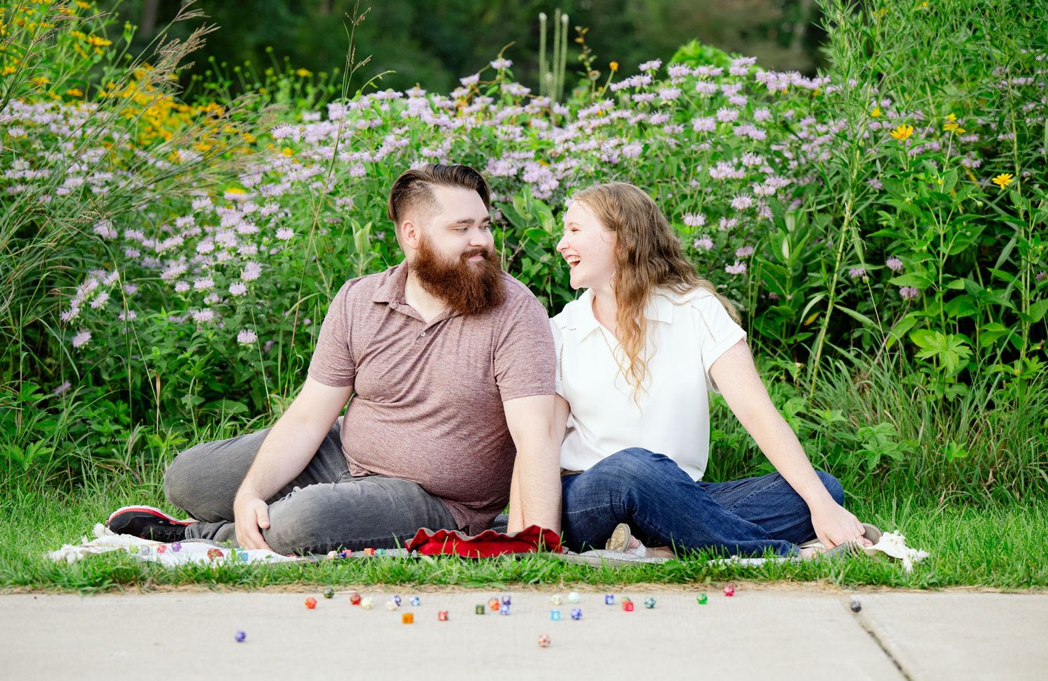 Couple relaxing on blanket amid pink wildflowers in a peaceful garden setting.