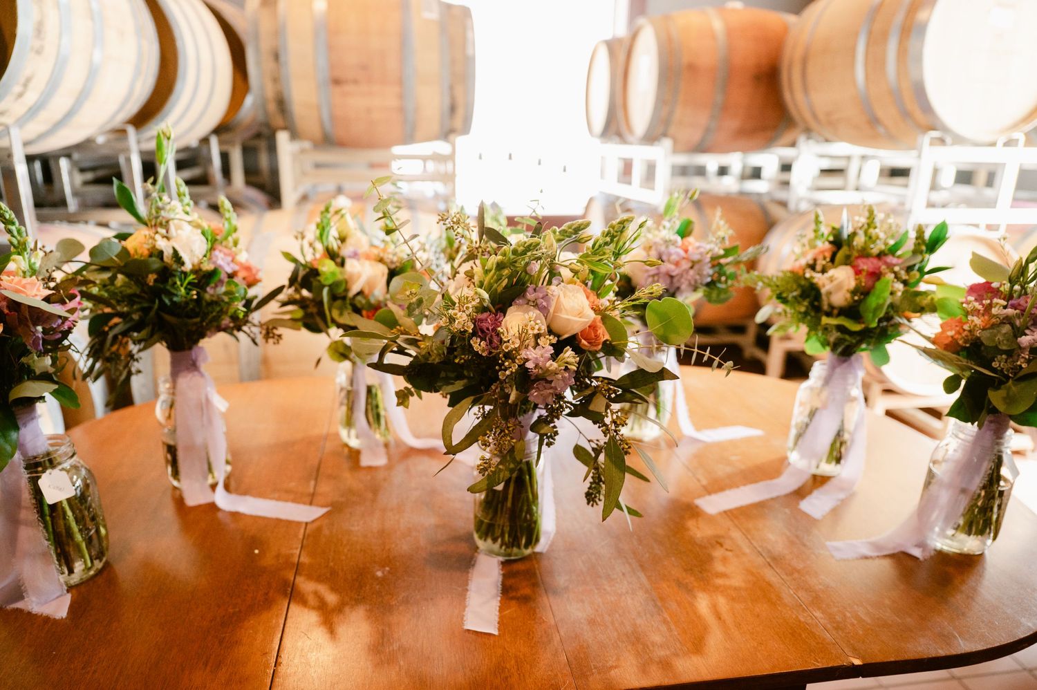 Wedding reception table settings with elegant white floral centerpieces on a long wooden farmhouse table.