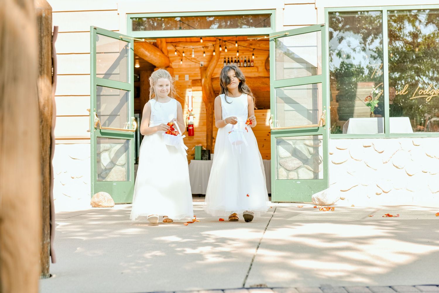 Wedding party members pose in front of a light-filled venue with large windows.