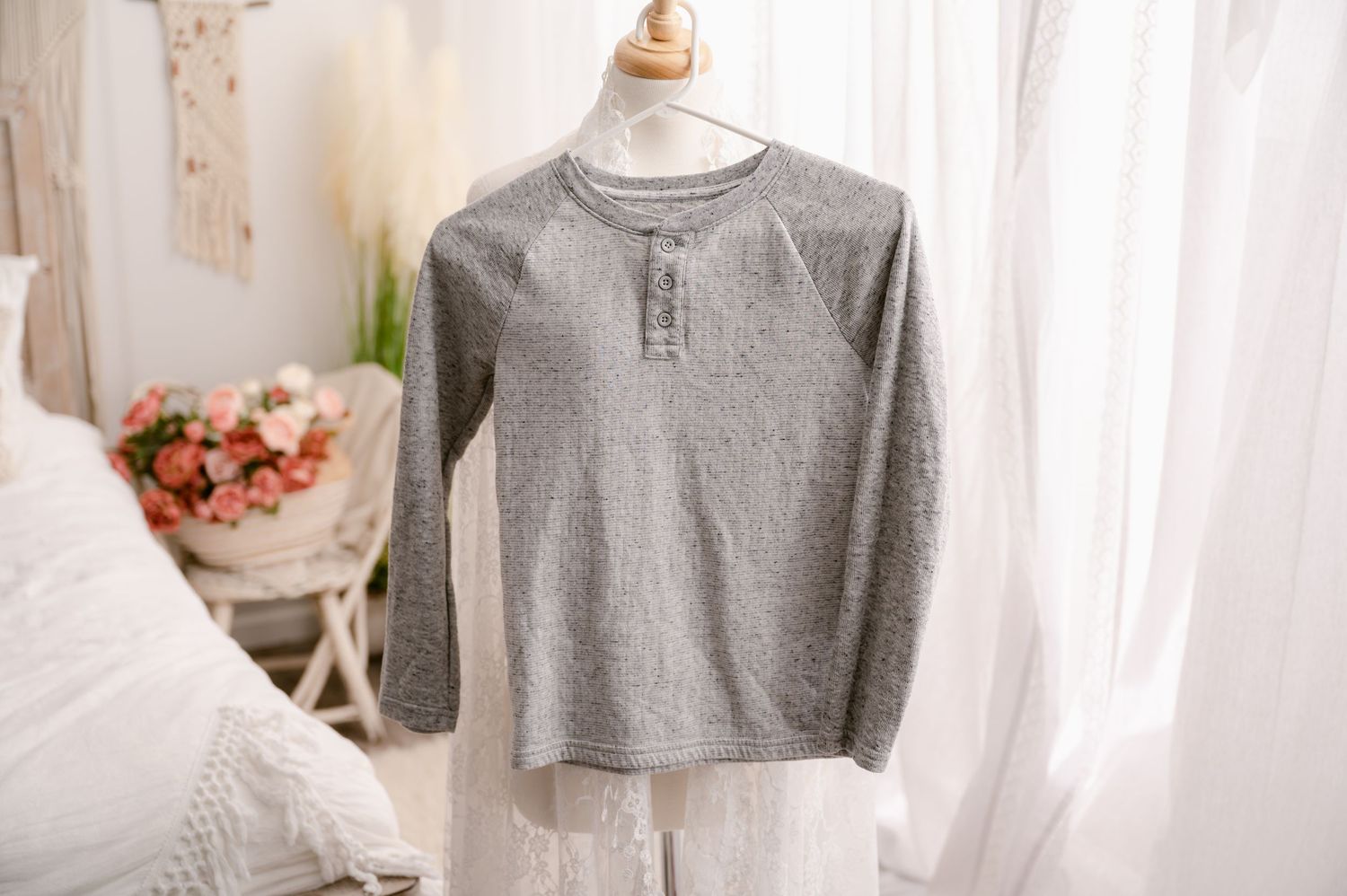 A casual gray henley long sleeve shirt displayed on a white mannequin torso against sheer curtains and floral decor.