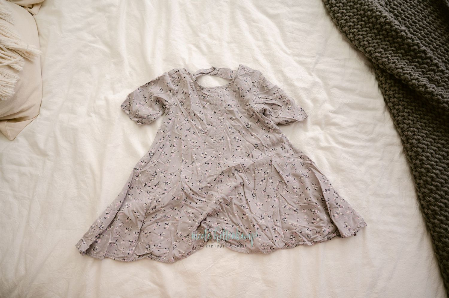 A vintage-style lace dress in pale gray lies flat on white bedding showing its delicate pattern and short sleeves.