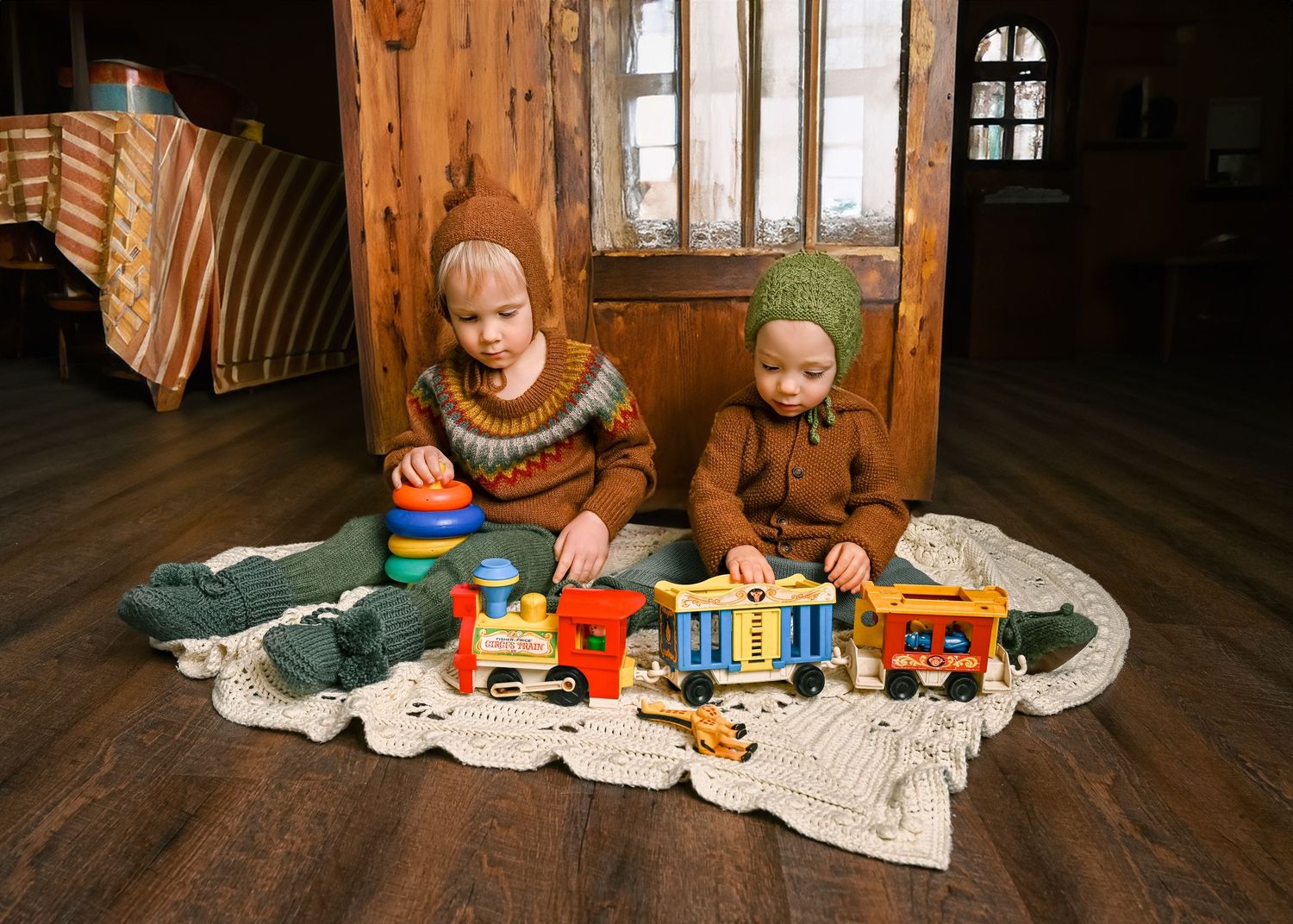 Two children play with colorful wooden toy trains on a blanket in a rustic wooden room.