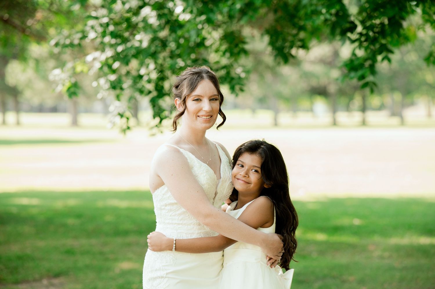 Bride in a white dress embraces her groom in front of a garden setting with green foliage.