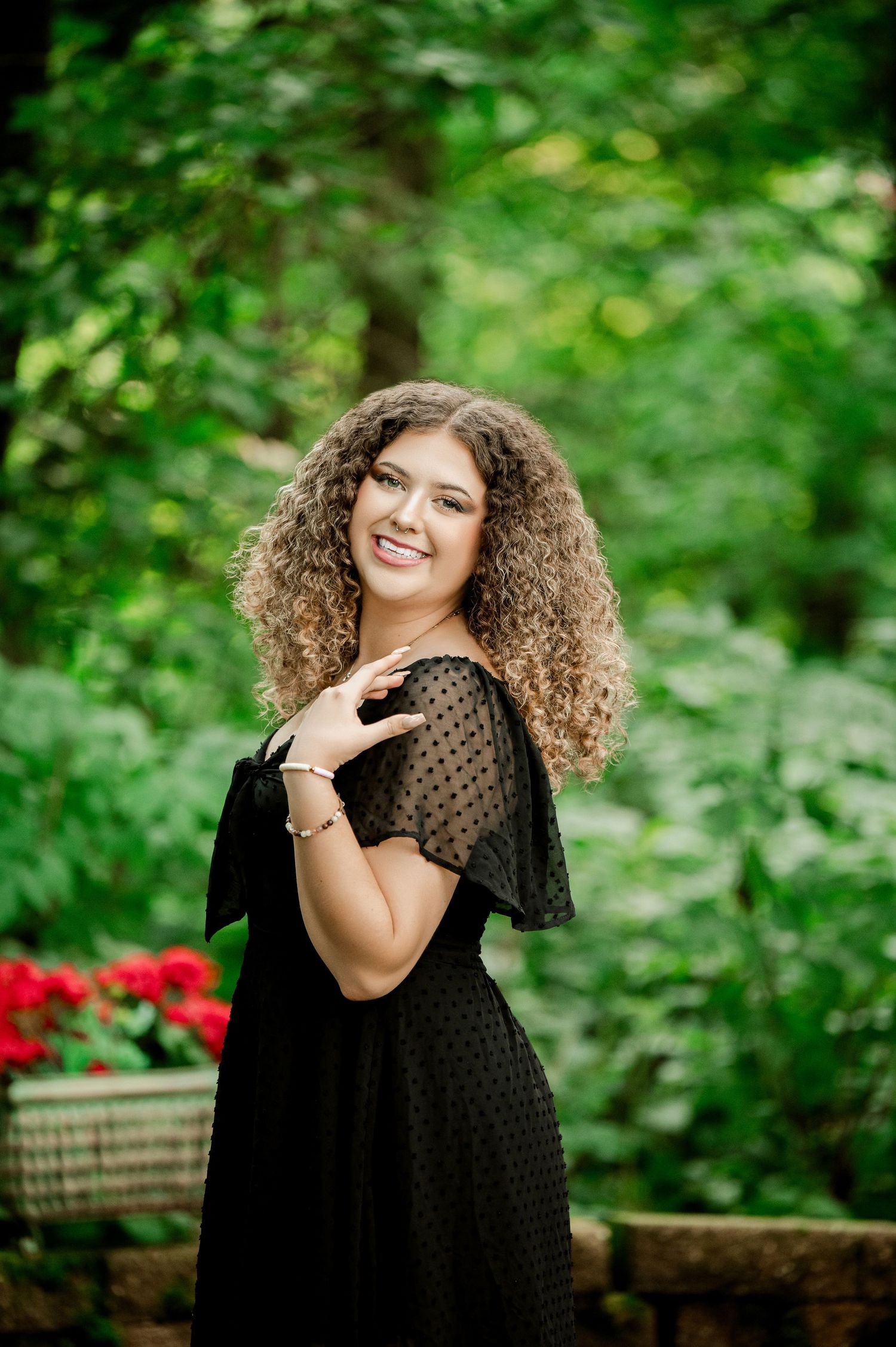 Joyful portrait against greenery wearing black polka dot dress and natural curls.