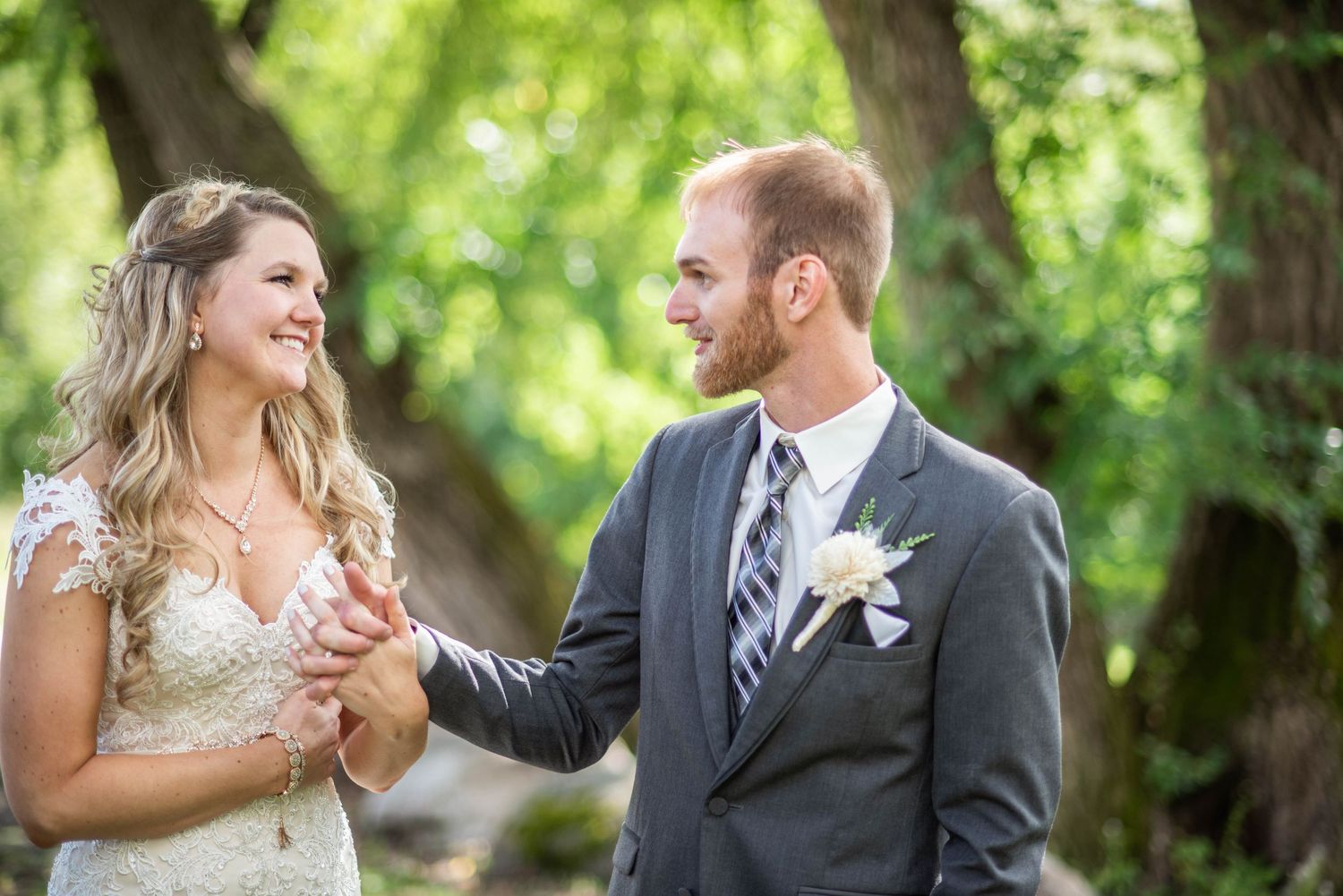 Wedding couple dances and laughs together under the shade of summer trees.