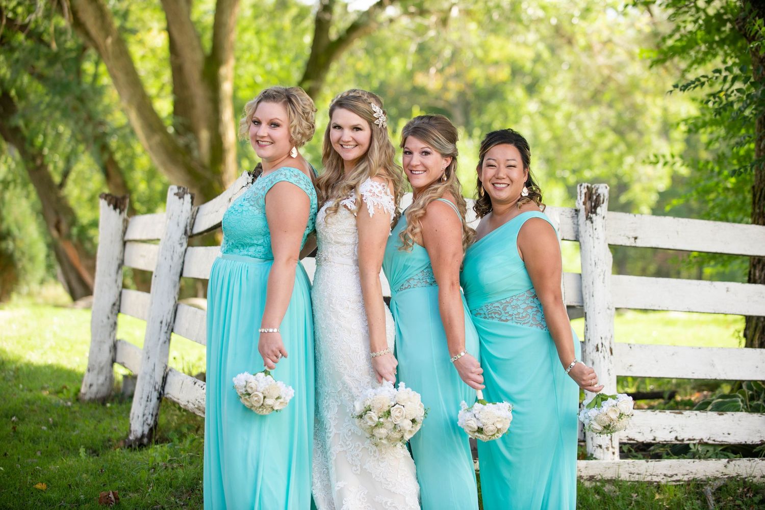Bridesmaids in matching turquoise dresses pose with the bride against a white fence. Rum River Barn Milaca Minnesota Weddings