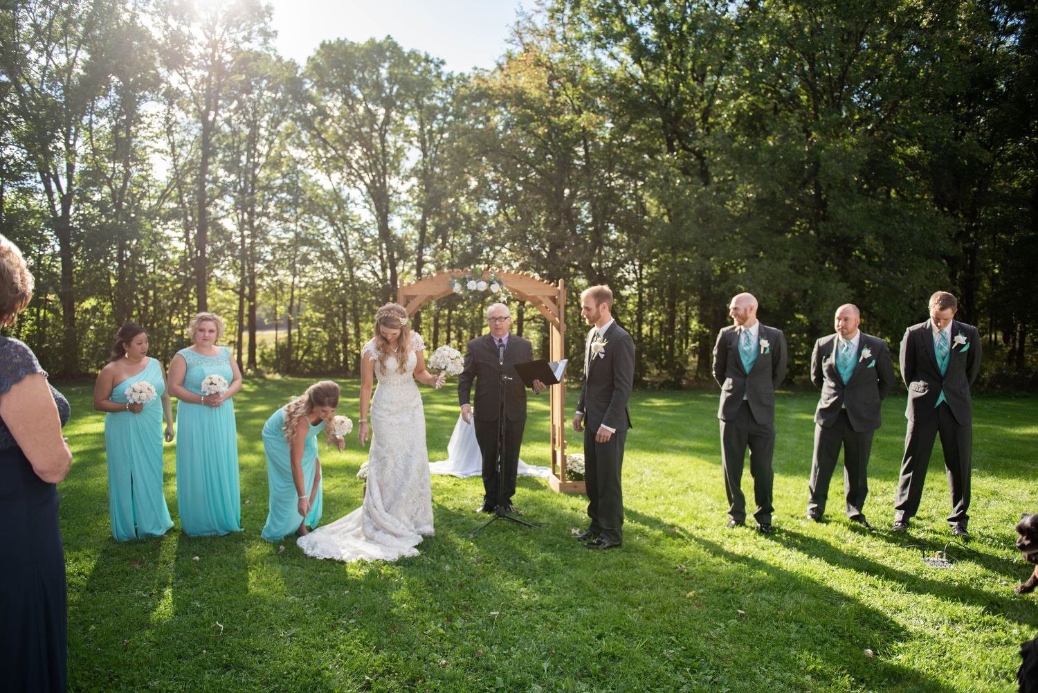 Wedding party gathered on a sunny lawn with bridesmaids in turquoise dresses and groomsmen in dark suits. Rum River Barn Milaca Minnesota We
