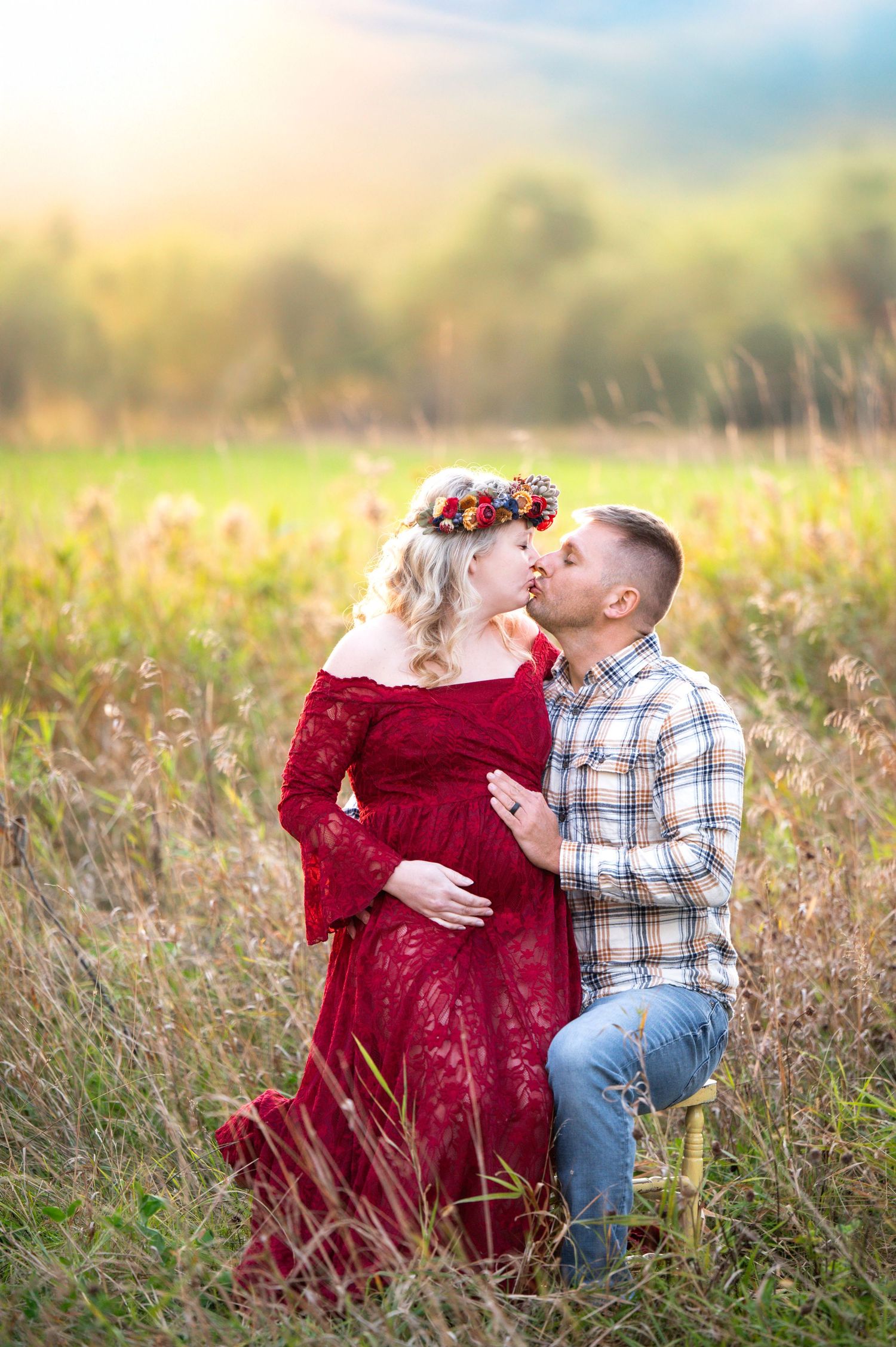 A maternity photo of a couple in a field at sunset, with the woman wearing a red lace dress.