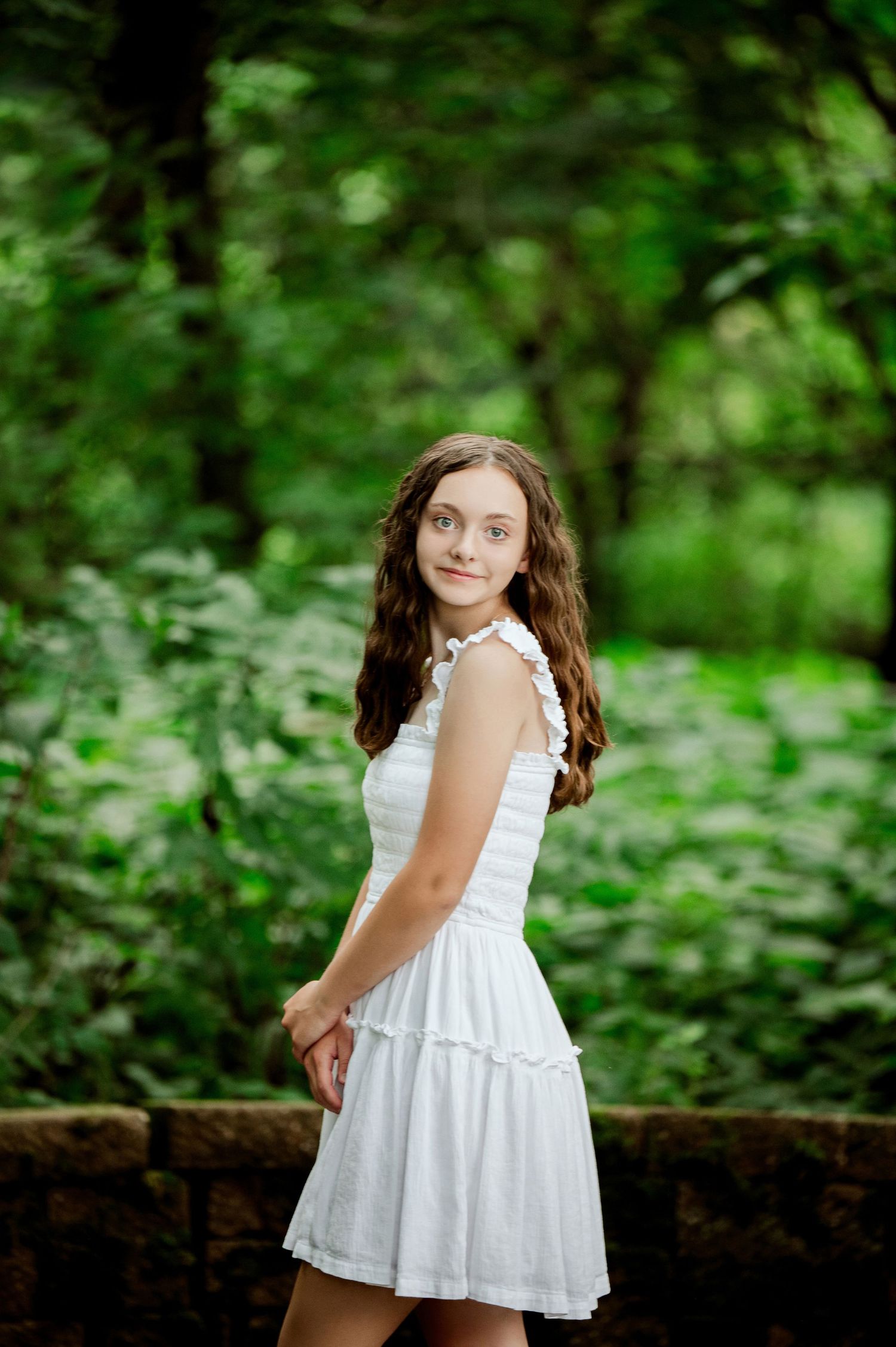 Summer portrait session in white dress against natural stone wall and greenery.