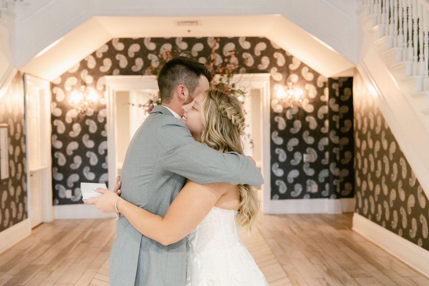 Couple shares their first dance in an elegantly decorated room with geometric wallpaper.