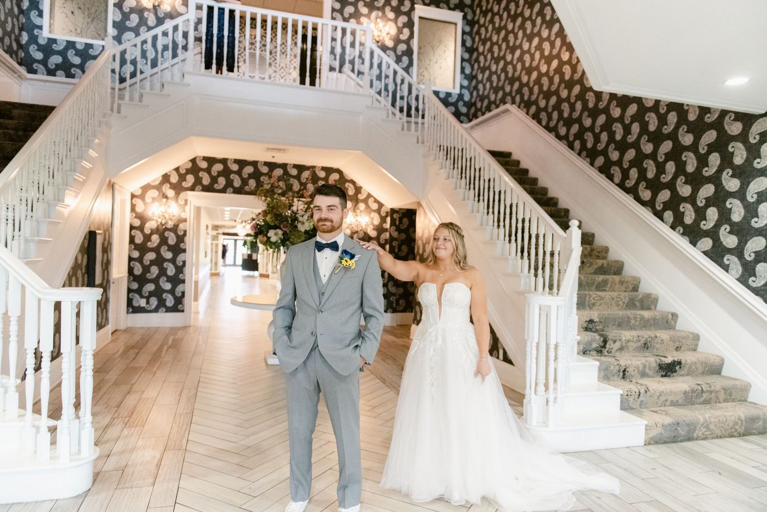 An elegant wedding venue interior features a grand white staircase and patterned wallpaper.