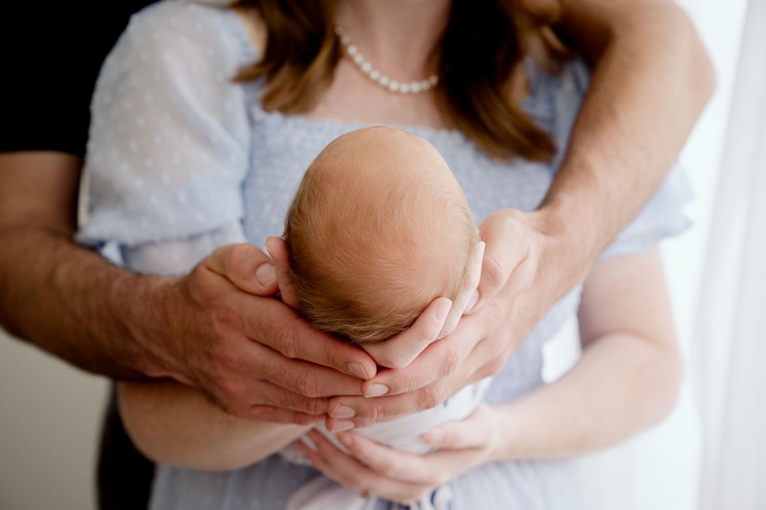A tender newborn photography session with hands cradling a small baby's head.
