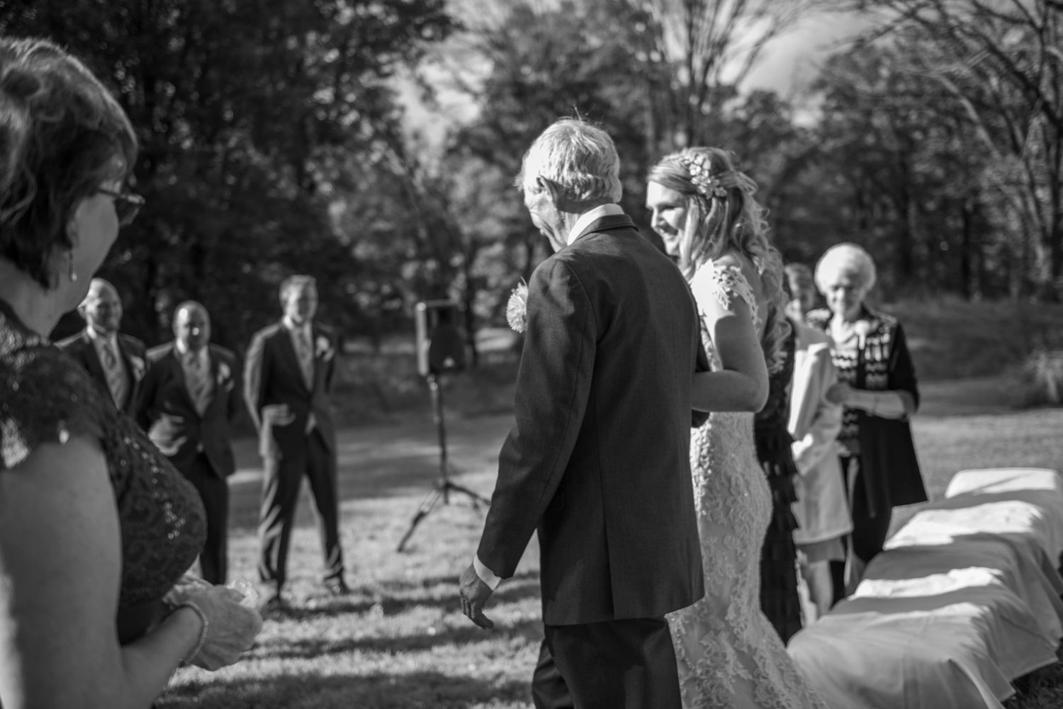 Black and white candid ceremony photo showing guests gathered outdoors for wedding proceedings. Rum River Barn Milaca Minnesota Weddings