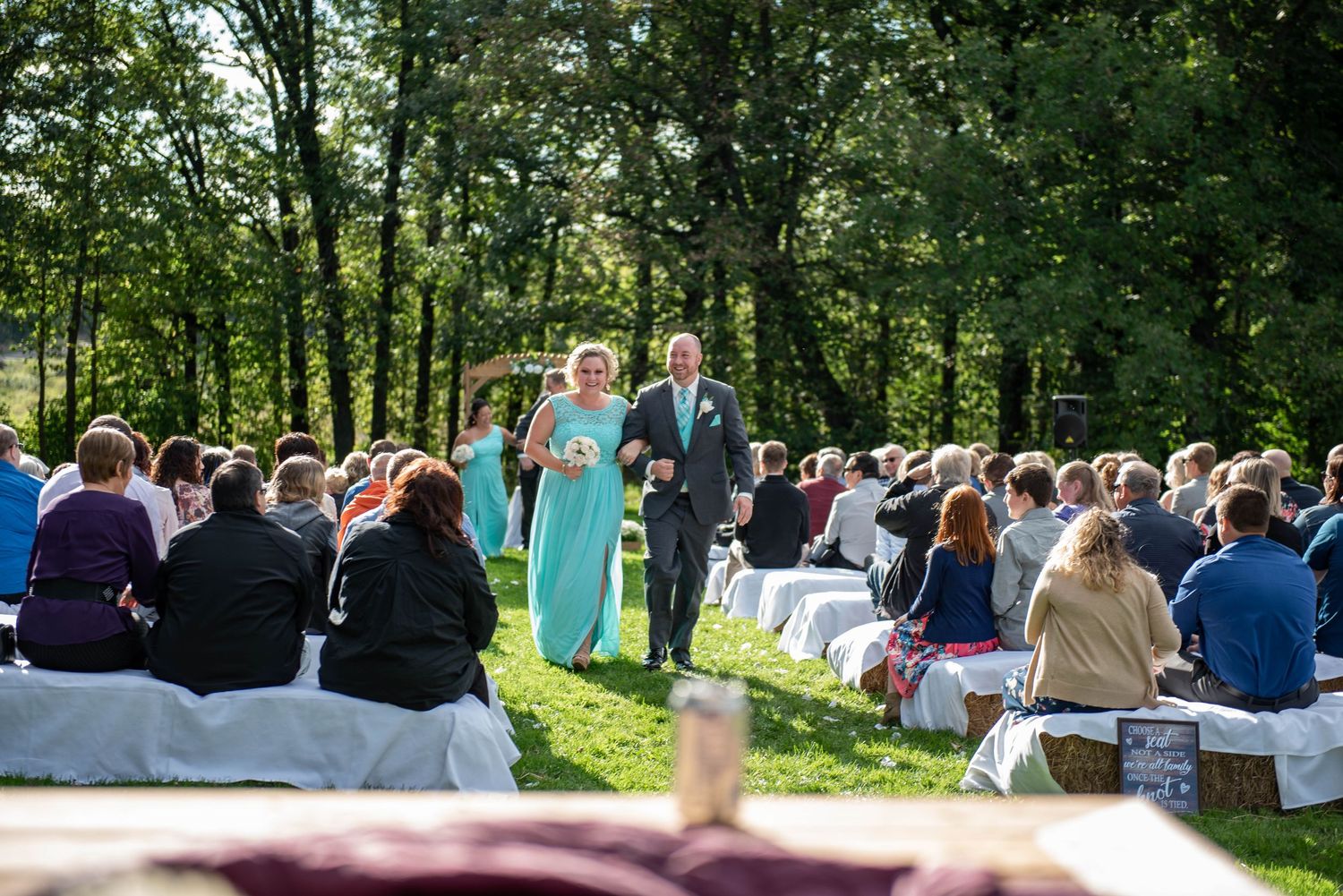 Outdoor wedding ceremony in wooded setting with guests seated on white chairs. Rum River Barn Milaca Minnesota Weddings