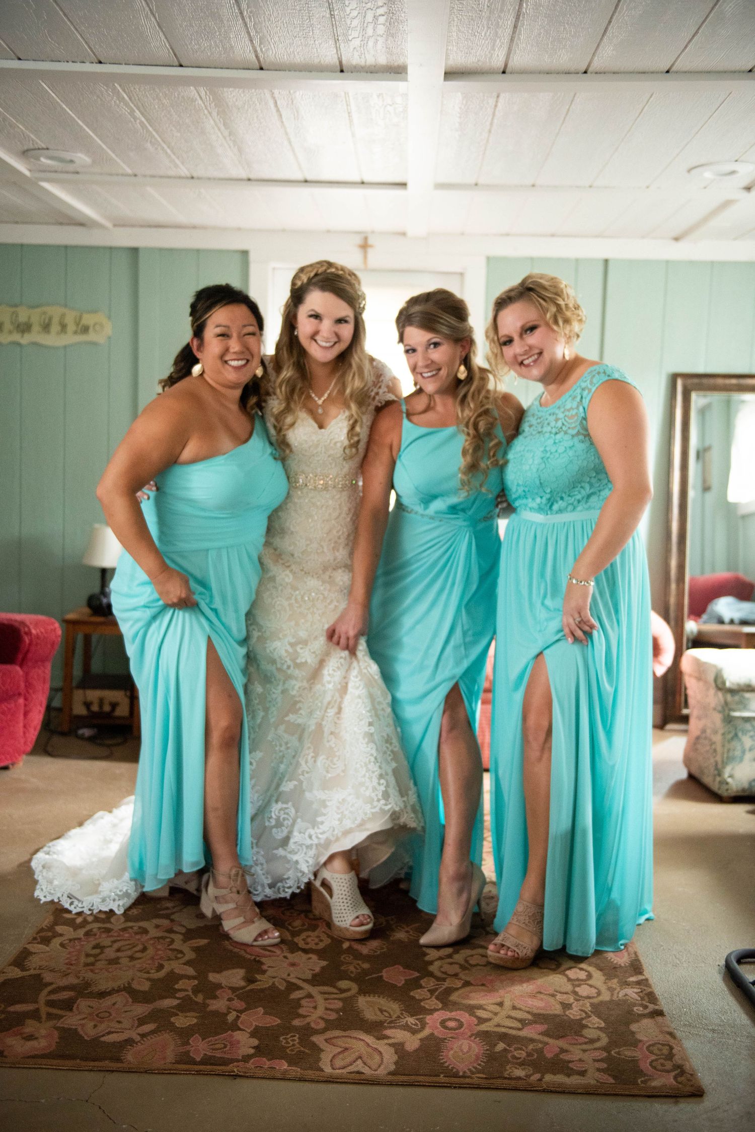 Wedding party poses together in matching turquoise bridesmaid dresses and white lace bridal gown in interior setting. Rum River Barn Milaca