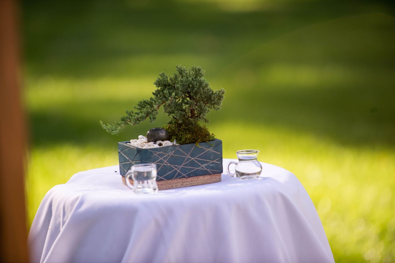 A small bonsai tree centerpiece sits elegantly on a white tablecloth in outdoor lighting. Rum River Barn Milaca Minnesota Weddings