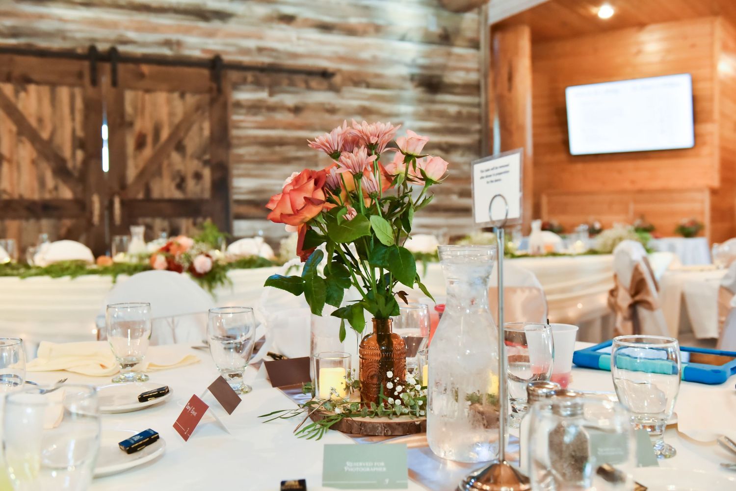 Rustic wedding reception tables lined up in a wooden barn venue with vintage decor.