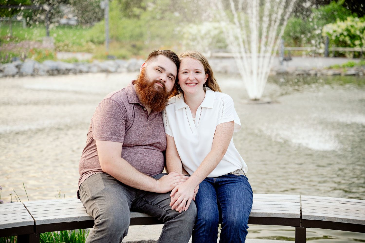 St cloud area engagement photo people sitting close together on a wooden deck overlooking a pond with a water fountain in the background.