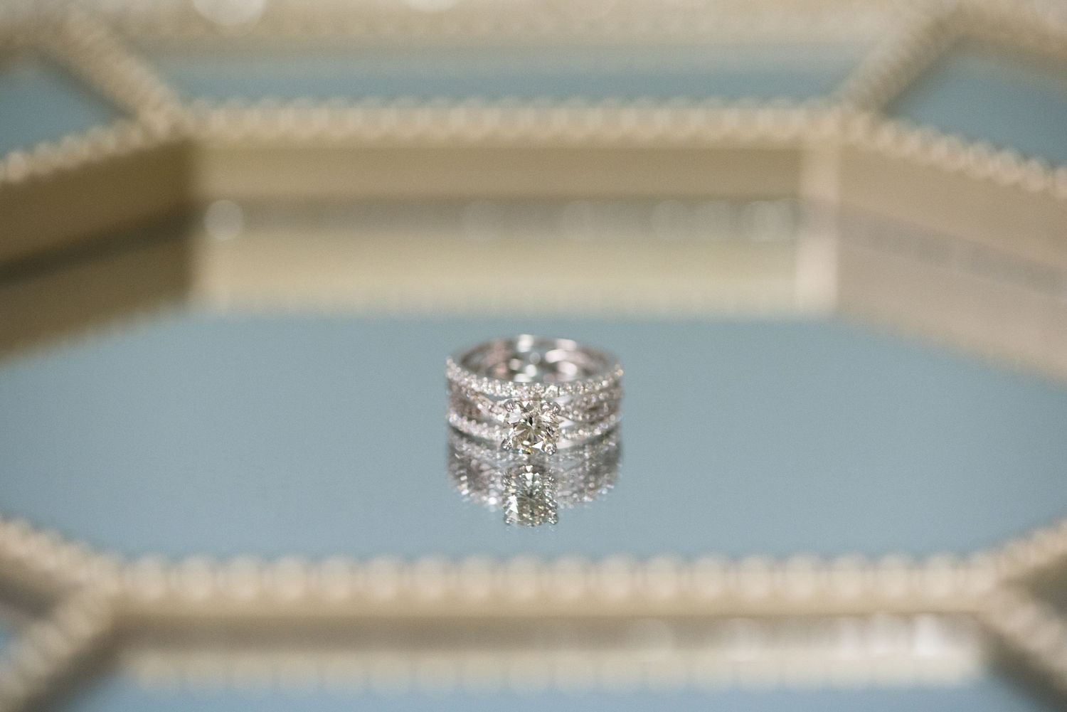 Wedding rings displayed on a cream-colored textured surface with shallow depth of field. Andover wedding at Magestic Oaks Golf Club