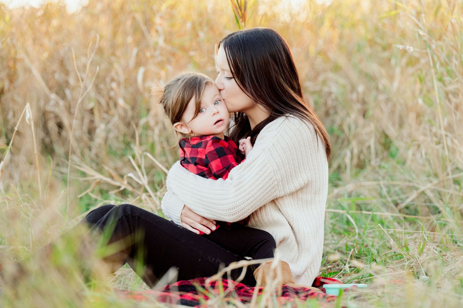 Sweet candid moment between mother and child sitting in golden grass field wearing cozy sweaters. Princeton MN Milestone, Maternity and Newb