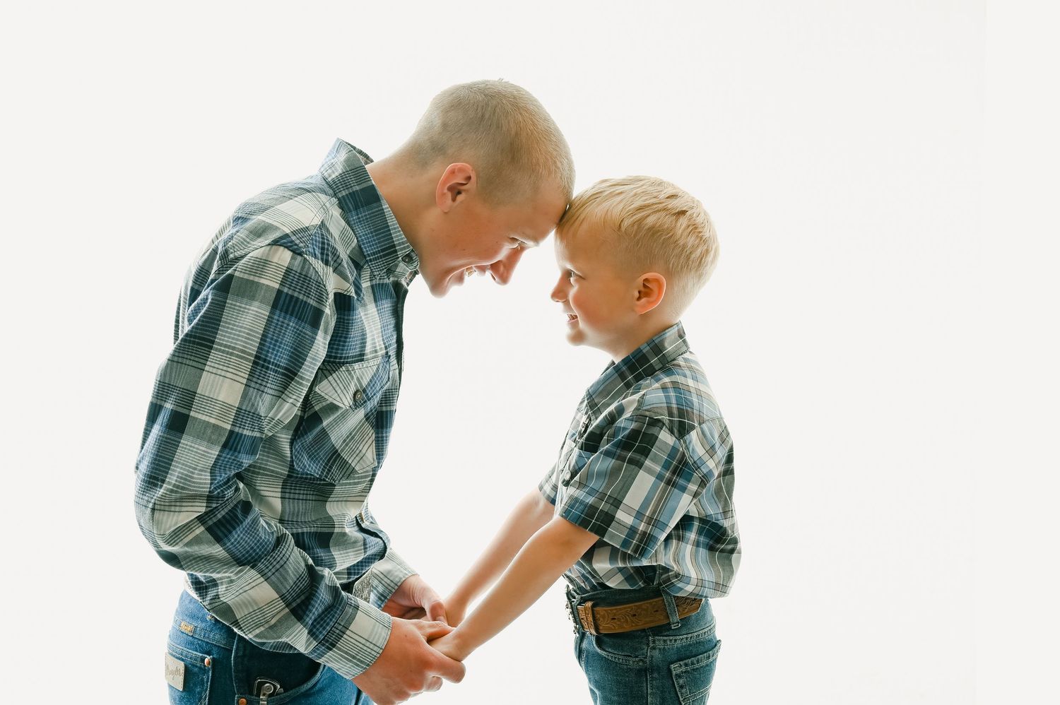 A parent and child wearing matching plaid shirts stand facing each other in a tender moment against a white background.