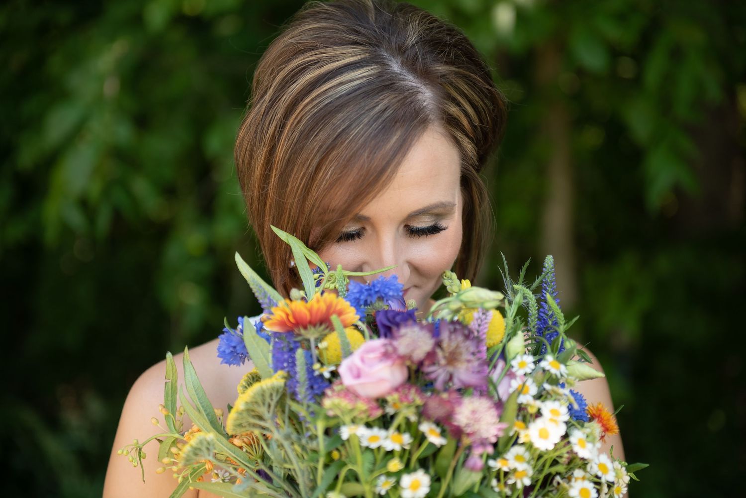 A person holds a vibrant bouquet of mixed flowers in a natural outdoor garden setting.
