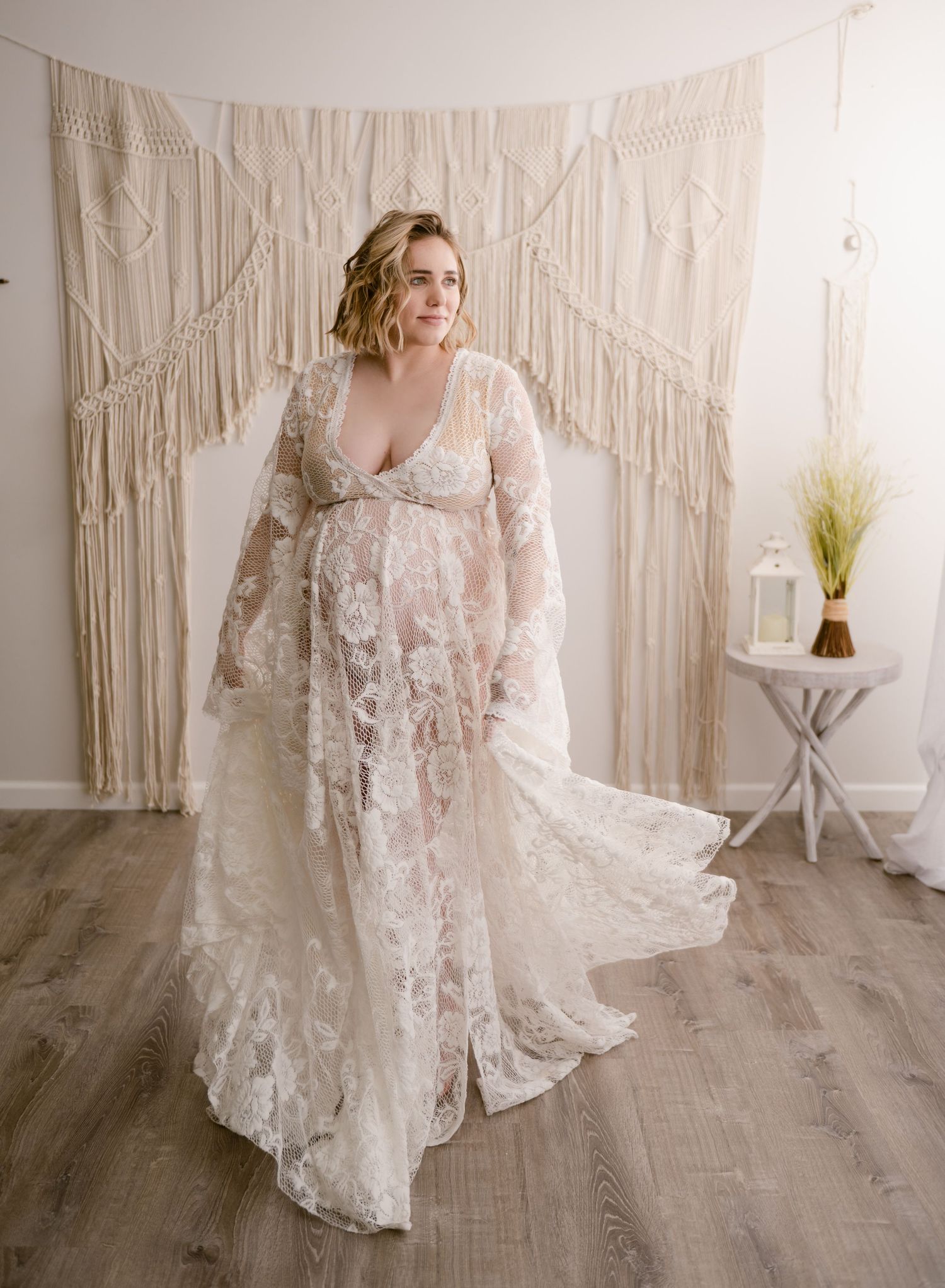 White lace wedding dress with long sleeves and train photographed against macrame backdrop in natural light studio setting.