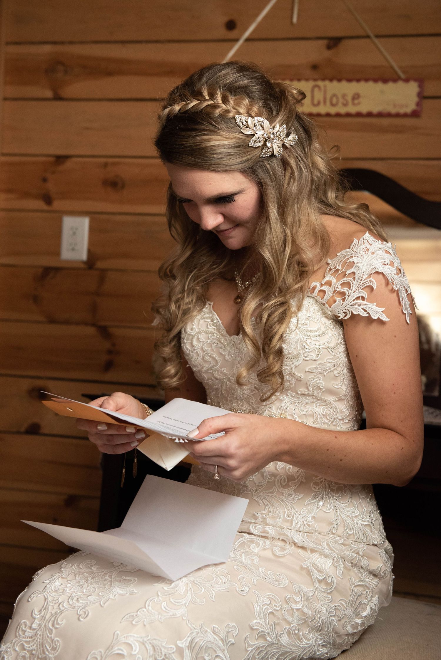 Person in lace wedding gown reads letter while sitting in rustic wooden room wearing leaf crown. Rum River Barn Milaca Minnesota Weddings