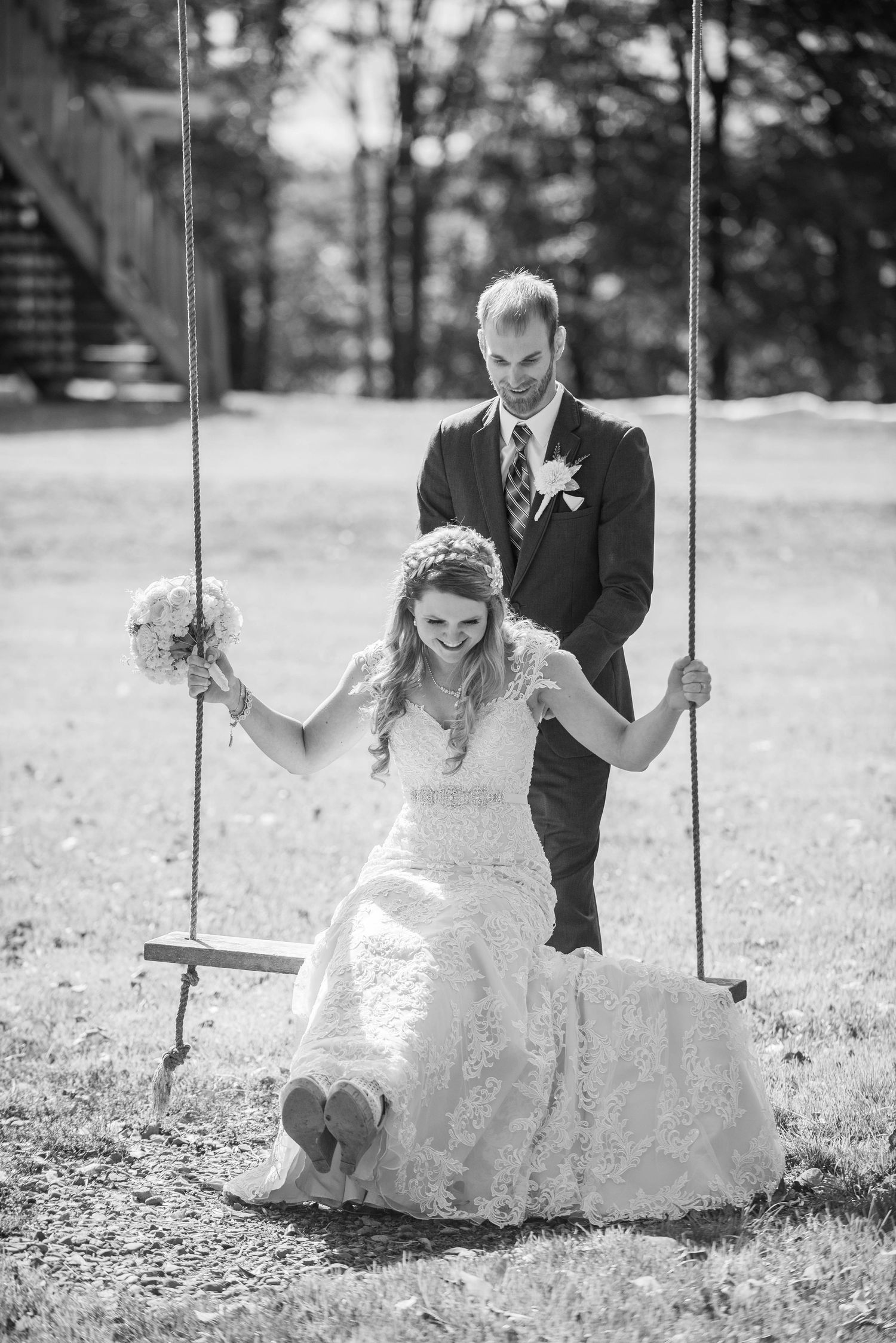 Black and white photo of a couple sharing a playful moment on a swing in formal attire. Rum River Barn Milaca Minnesota Weddings