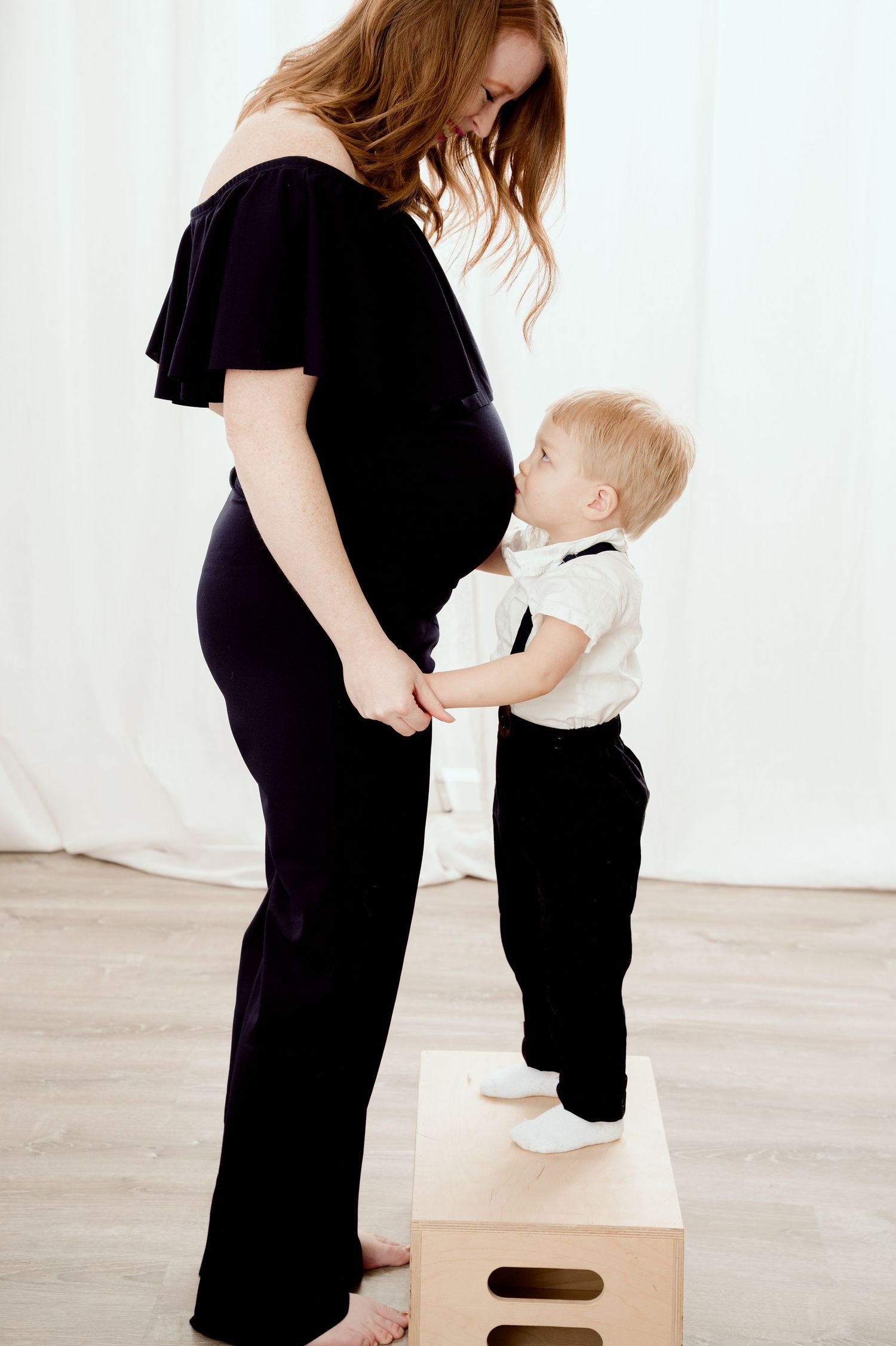 Two people in black and white clothing interact while one stands on a wooden box during a photo session.