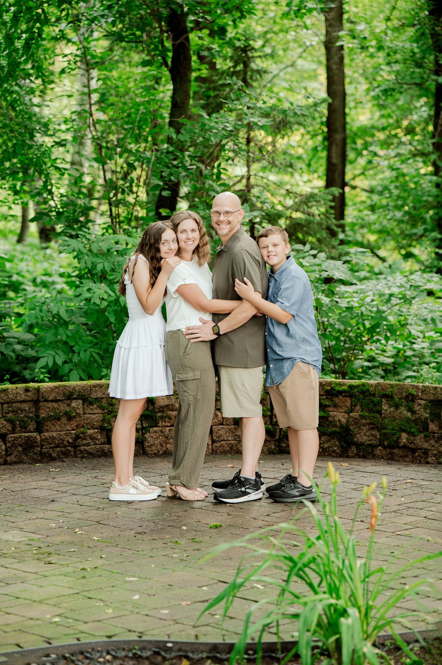 Clear Lake MN Family Photos: A casual family group photo taken outdoors on a stone patio surrounded by green forest scenery.