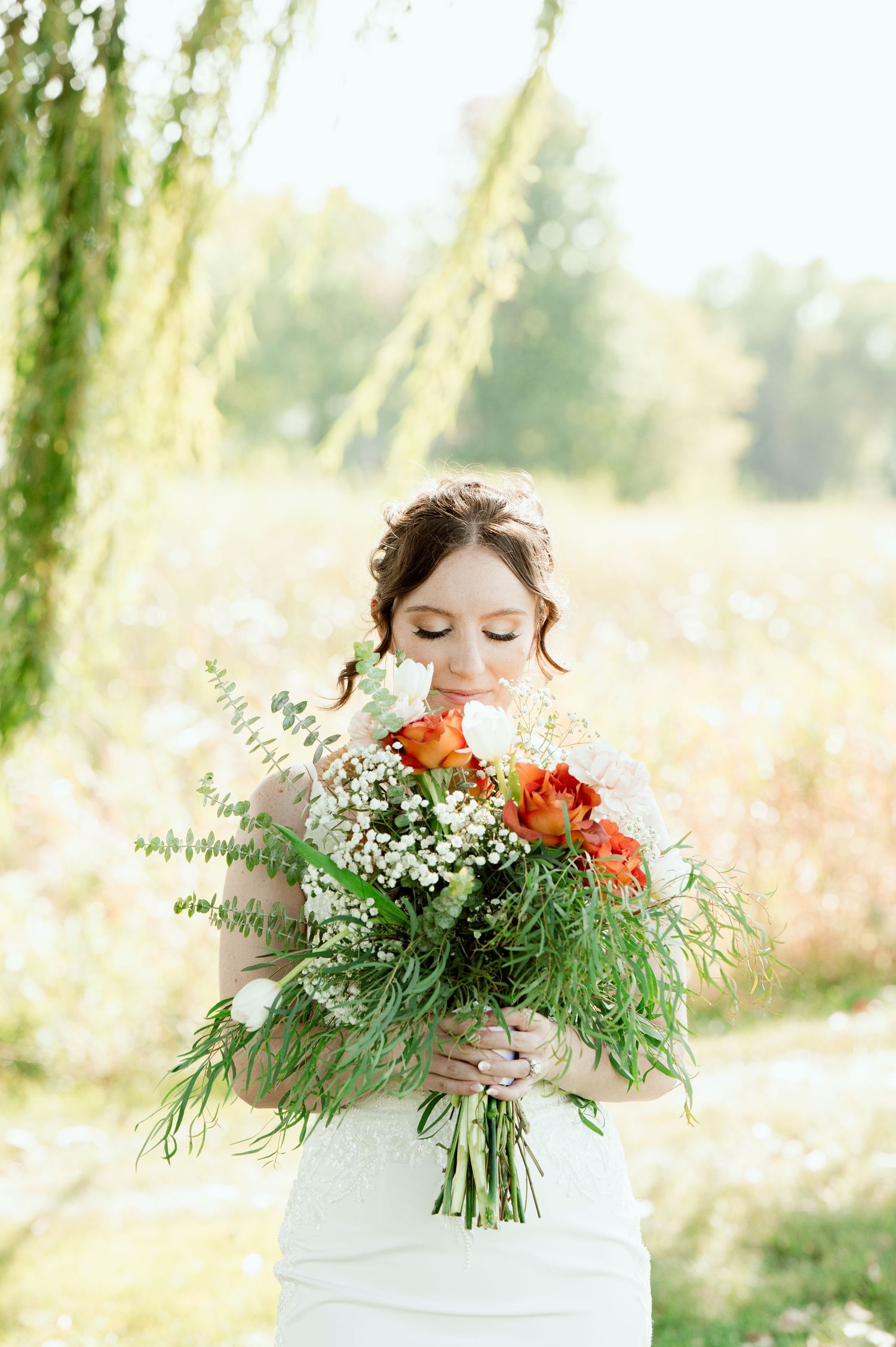 Bride holds a lush bouquet of orange flowers and greenery against a bright outdoor background.