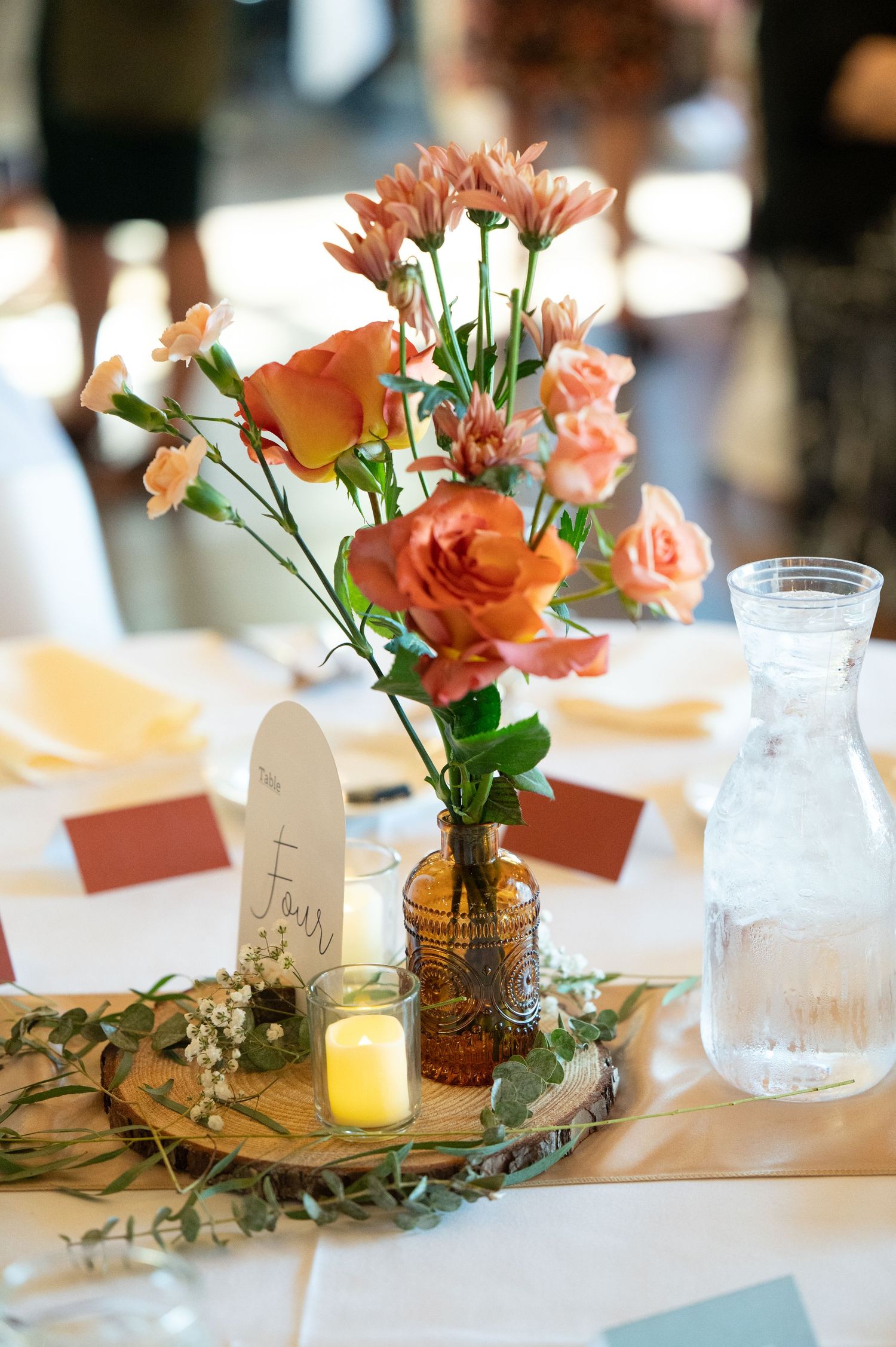 The Grands At Mulligans Elegant table centerpieces featuring coral roses in vases with tea lights and place cards at a wedding reception.